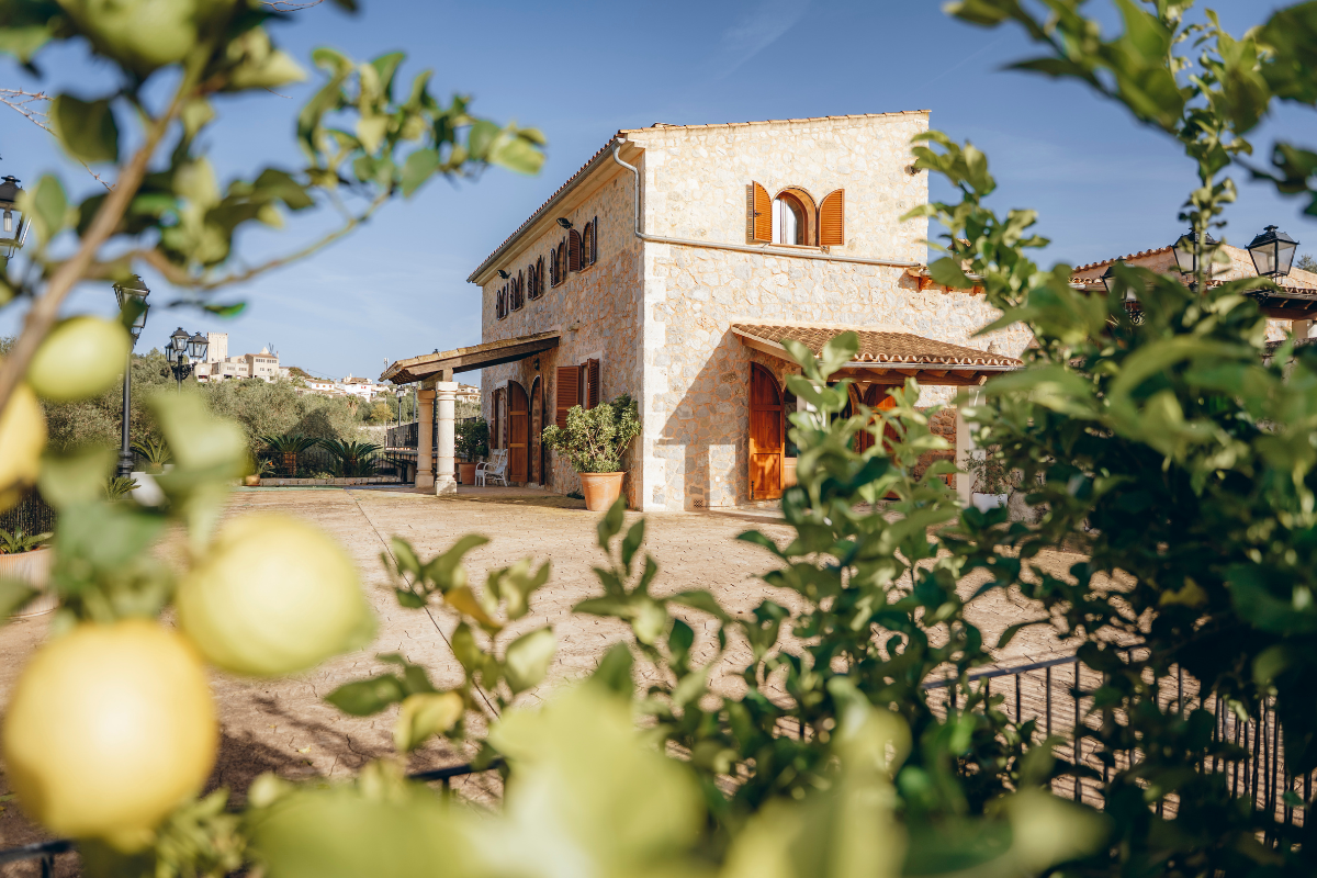 Ein Haus aus Stein mit Terrakottadach und Holztüren, umgeben von Zitronenbäumen, bei sonnischem Himmel.