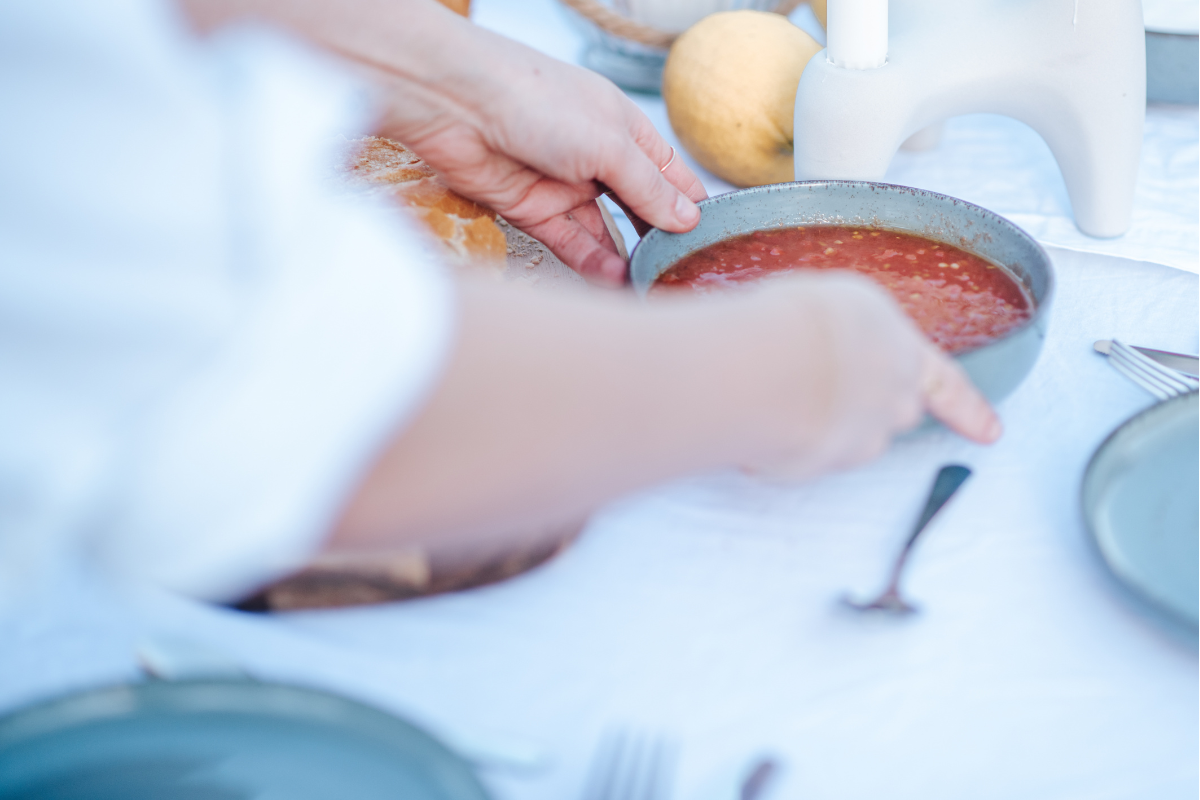 Person hält eine Schüssel mit roter Suppe oder Soße auf einem gedeckten Tisch