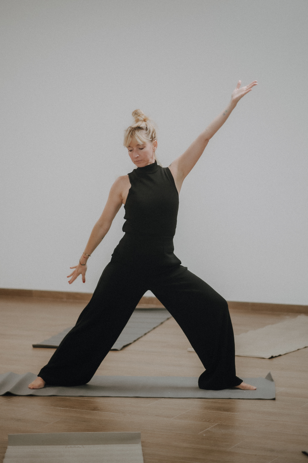 Frau beim Yoga in einem Raum mit Holzboden, trägt schwarze Kleidung und ist in einer seitlichen Dehnhaltung auf einer Matte.