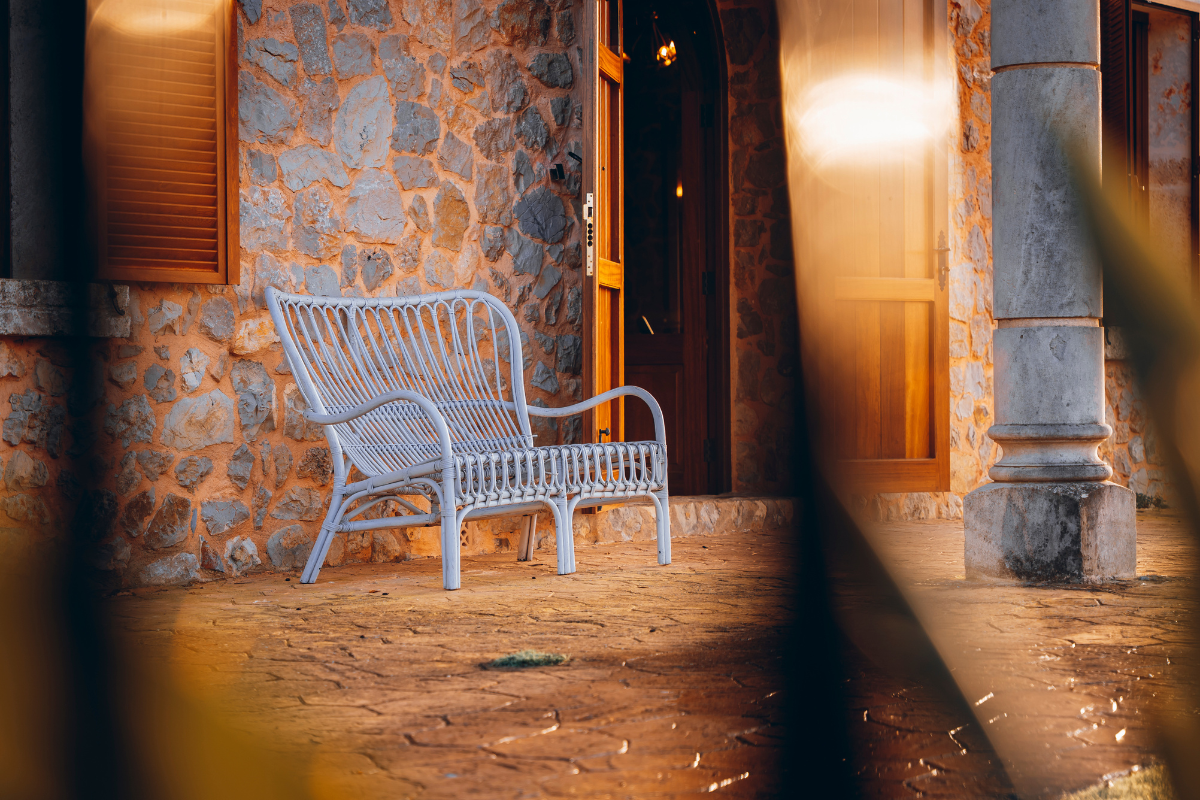 Ein weißes Gartenbank vor einer Steinwand und offenen Holztüren bei Sonnenuntergang.