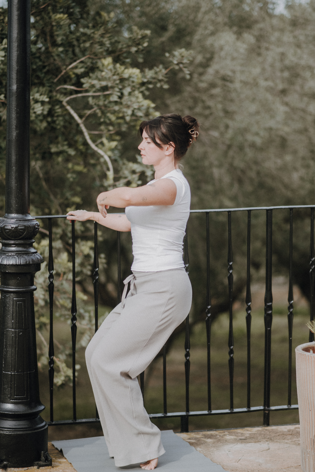 Frau beim Yoga im Freien, sitzend auf einer Yogamatte, umgeben von Bäumen.