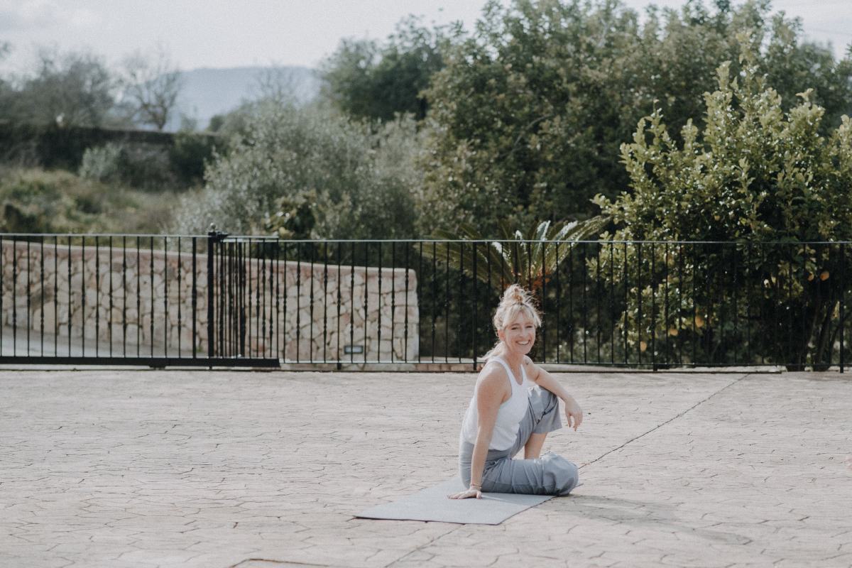 Frau macht Yoga im Freien auf einer Decke, umgeben von Bäumen und Pflanzen.