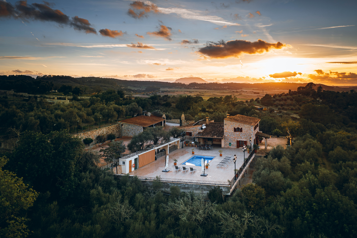 Ländliche Villa mit Swimmingpool im Sonnenuntergang, umgeben von Bäumen und Hügeln.