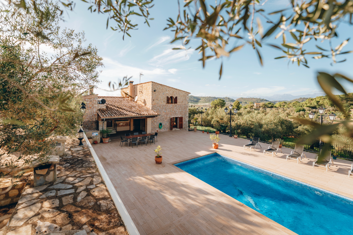 Ein Außenpool auf einer Terrasse vor einem rustikalen Steinhaus mit Balkon, umgeben von Sonnenliegen und einem Blick auf eine ländliche Region mit Bäumen und Hügeln.
