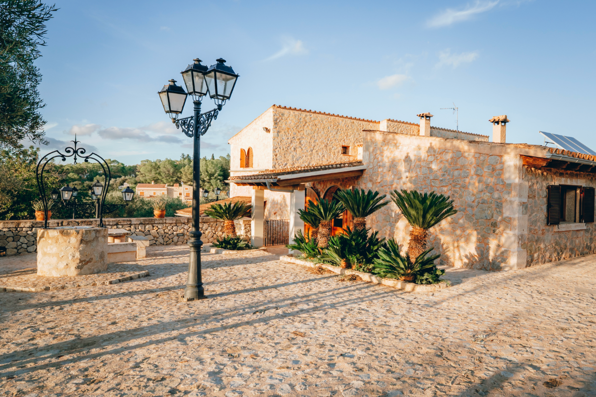 Ein Steinhaus auf einer sonnigen Terrasse mit Palmen und einem alten Laternenpfahl.