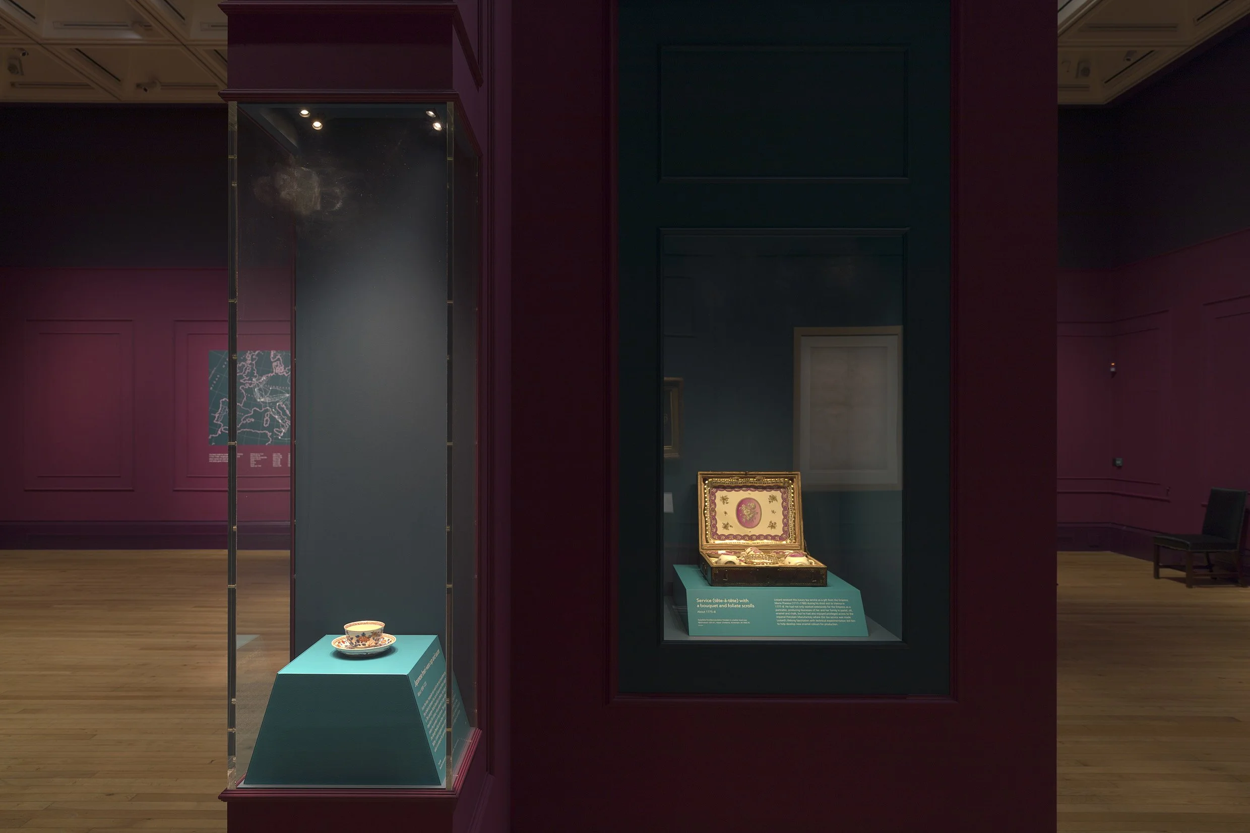 Museum display with a decorative box and a decorated bowl on teal pedestals, surrounded by purple walls.