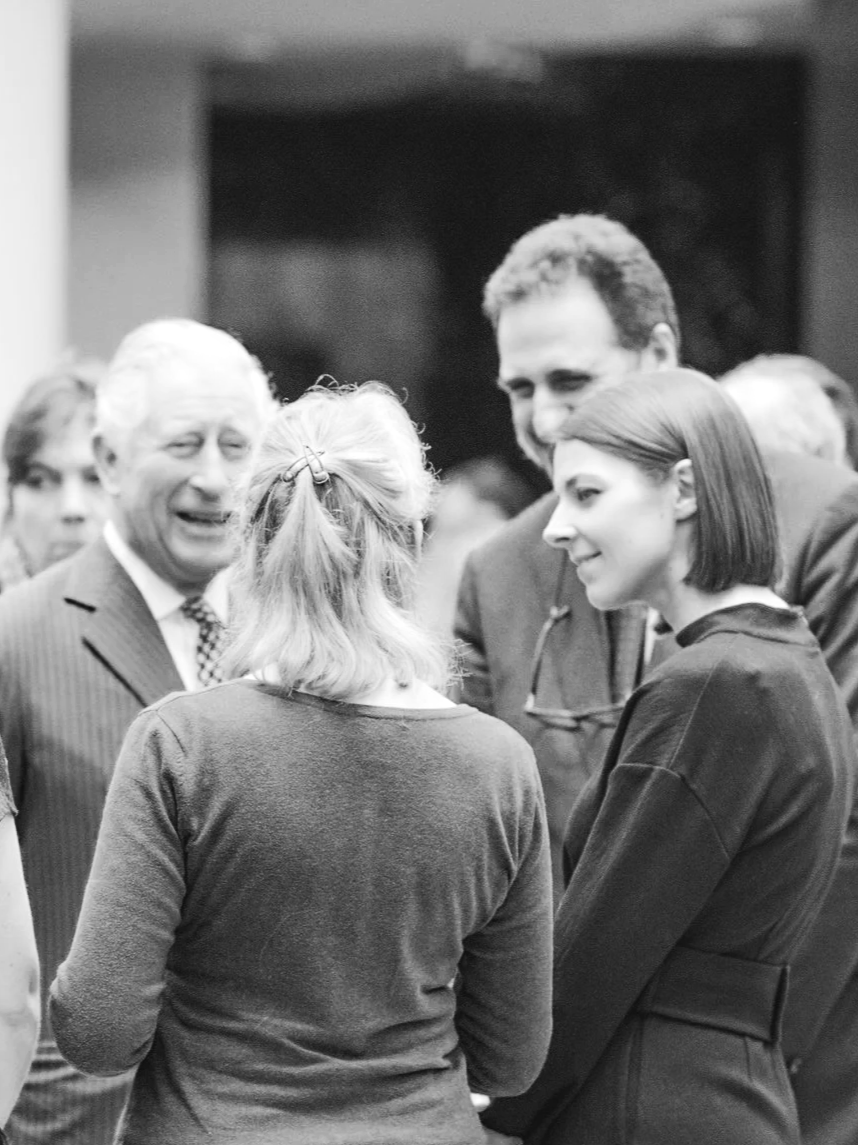 People engaged in conversation at a formal gathering or event, with men in suits and women in professional attire.