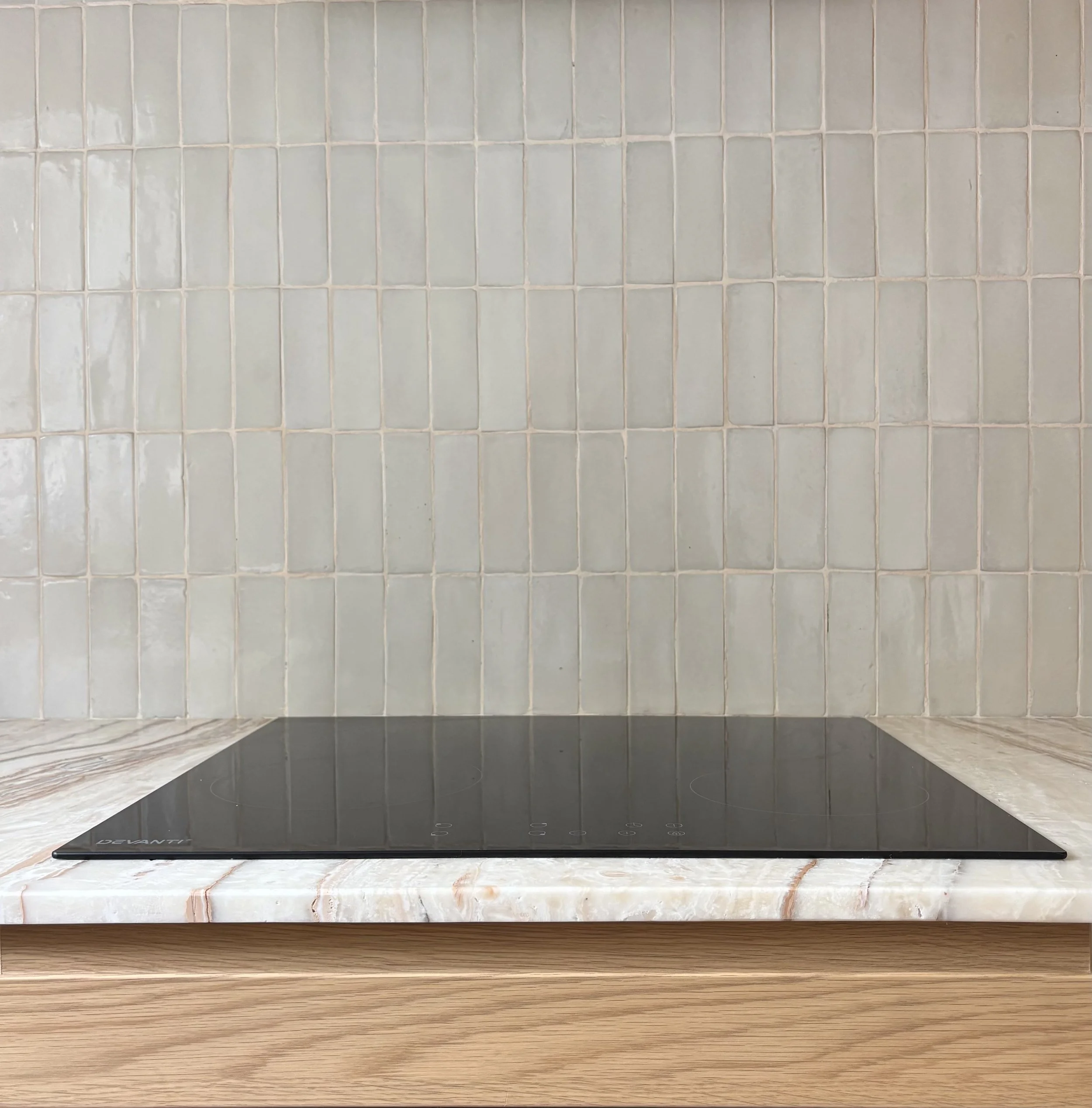A black induction cooktop installed on a marble countertop in front of a beige tiled backsplash.