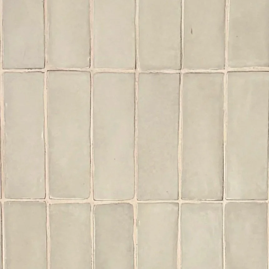 A close-up of a wall with light-colored square tiles and grout lines.