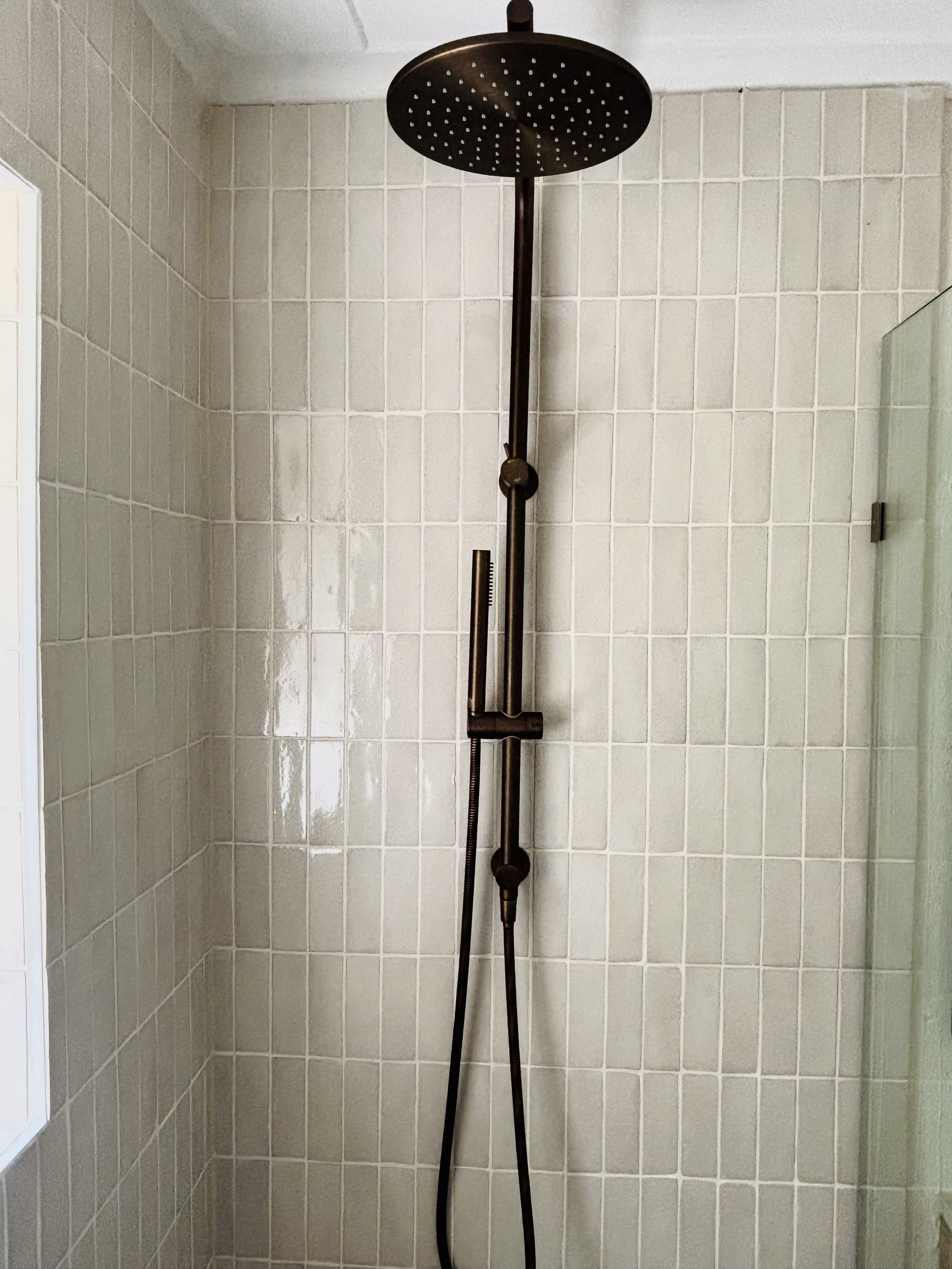 A modern showerhead mounted on a tiled wall with a handheld shower wand.