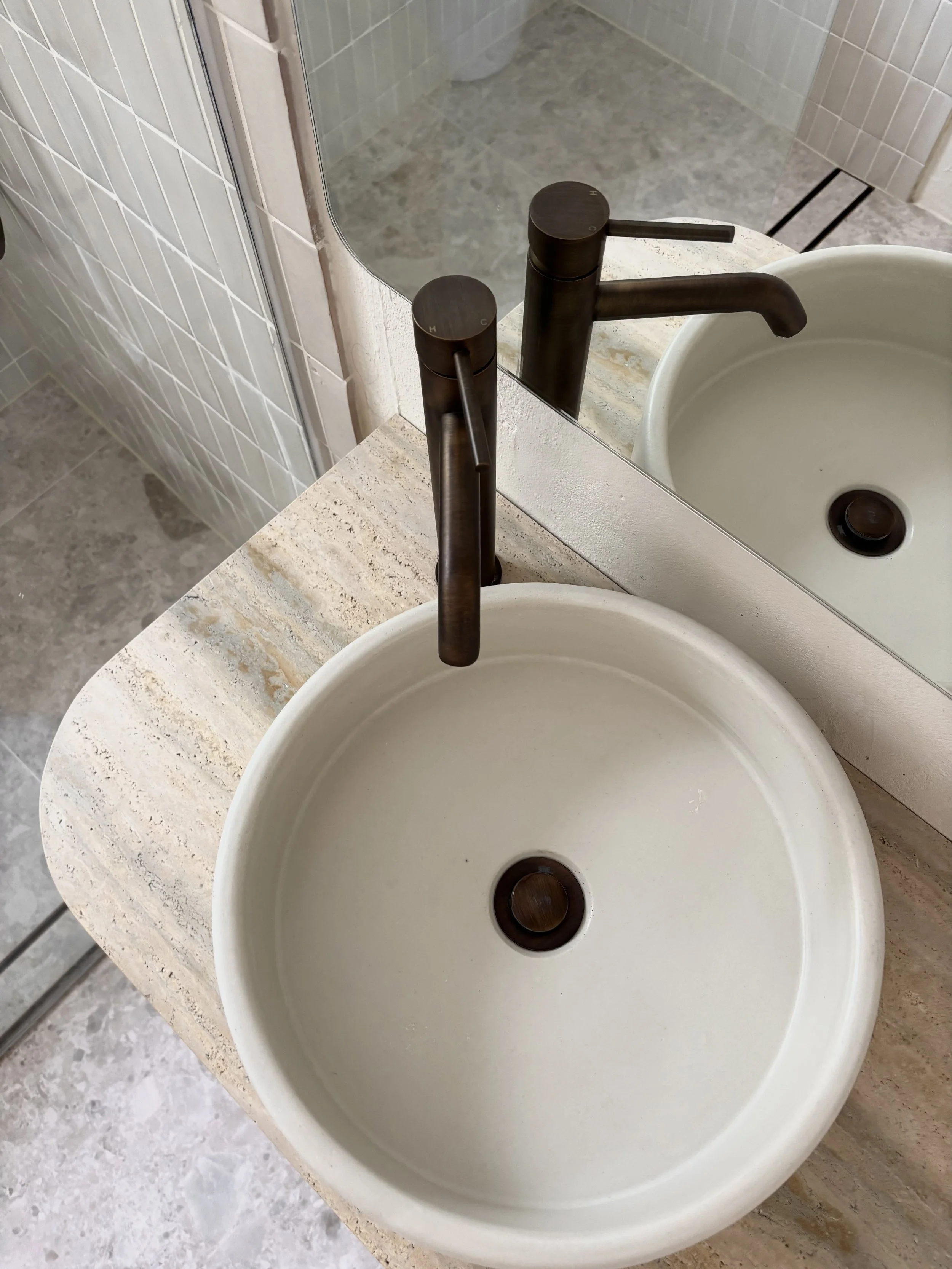 A round white bathroom sink with a modern black faucet mounted on a stone countertop, reflected in a mirror.