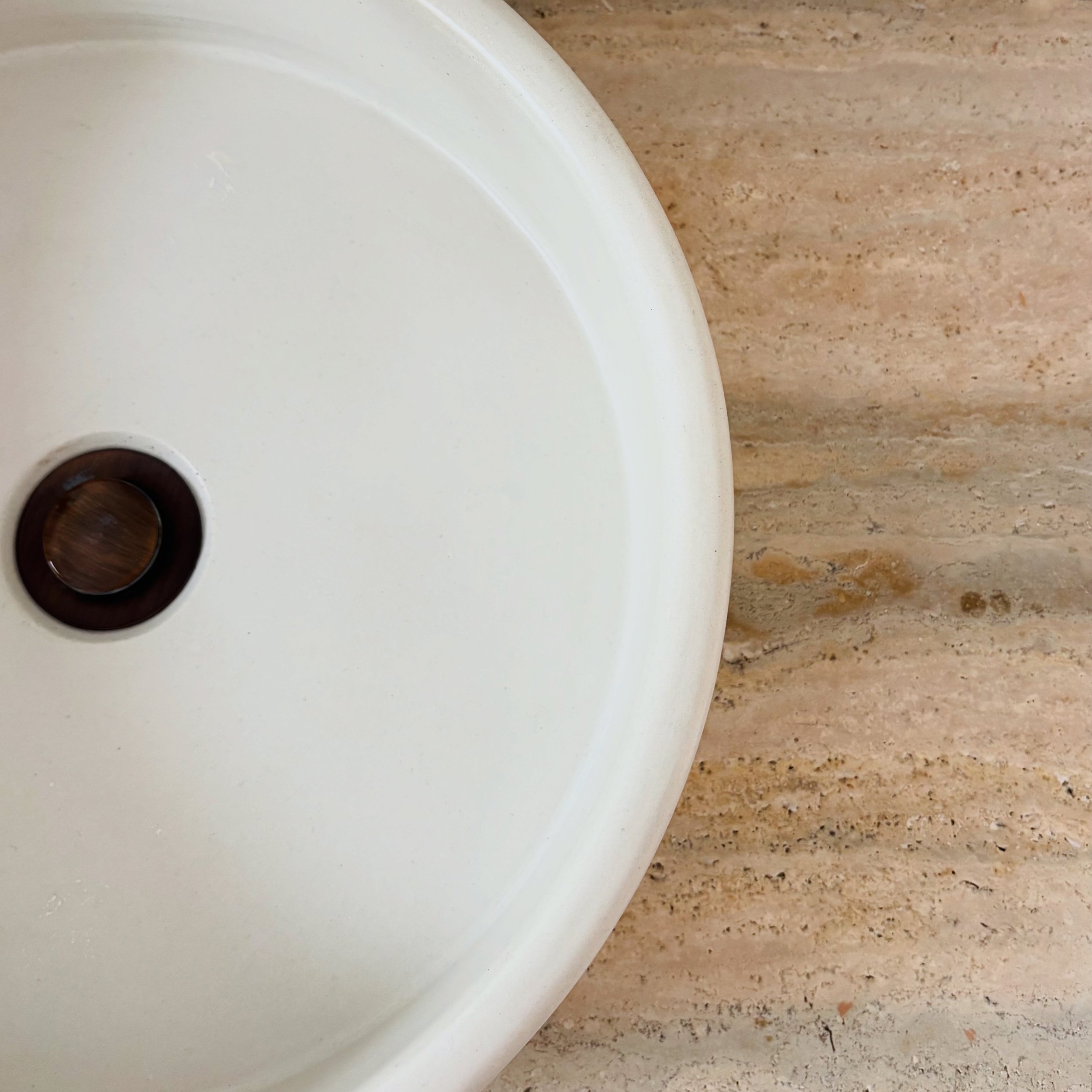 Close-up of a white sink basin installed on a beige marble countertop.