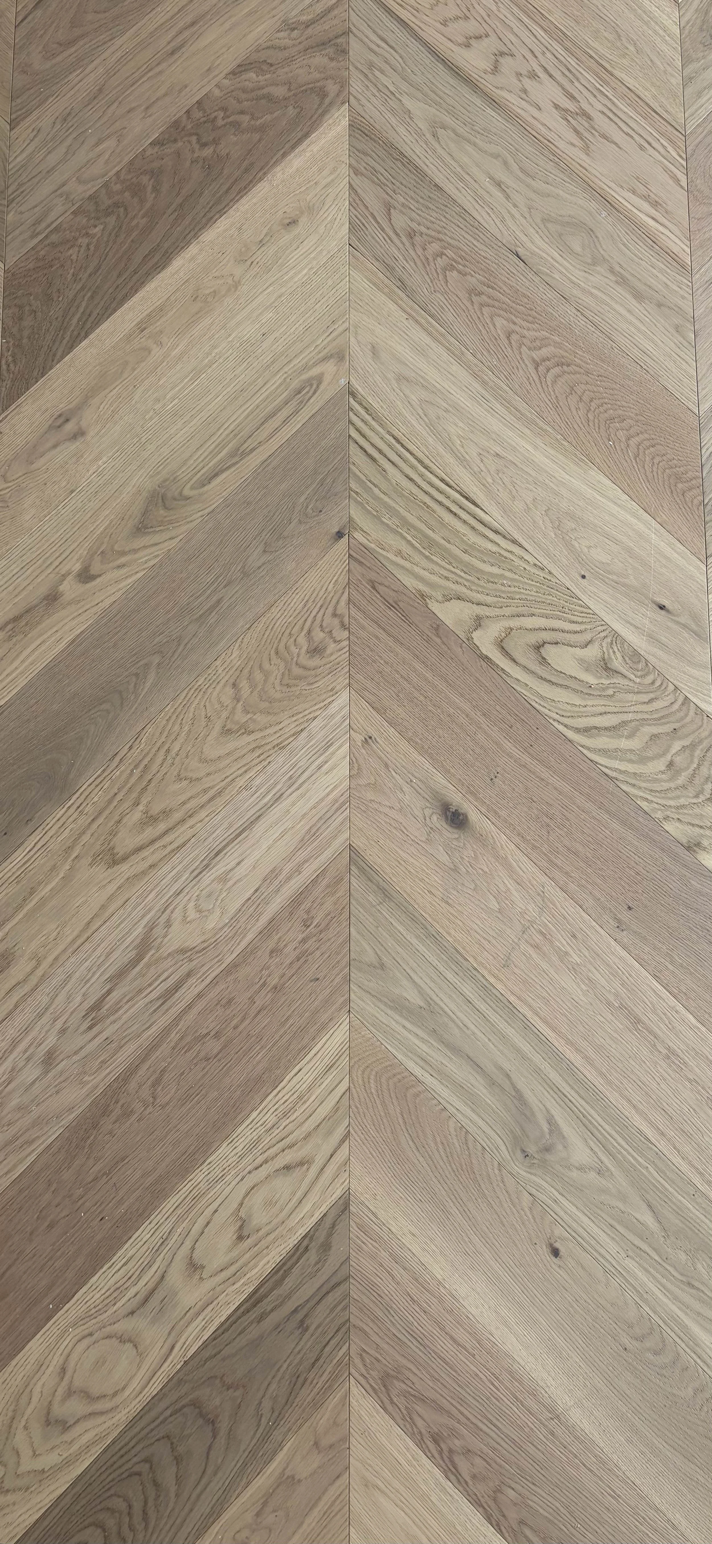 Wooden floor with a herringbone pattern, consisting of light and medium brown planks with visible grain and knots.