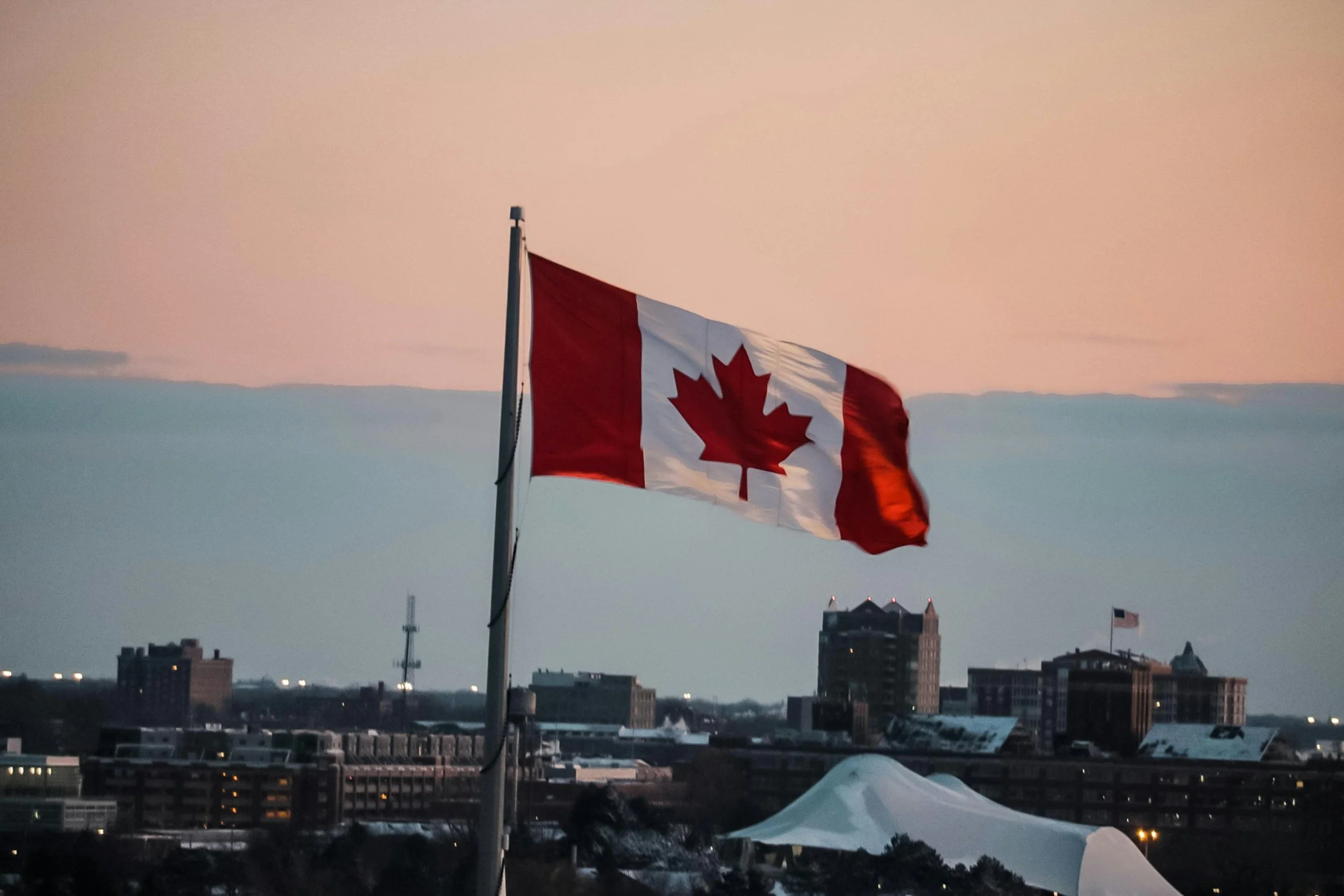 Canadian flag waving in the wind over a cityscape during sunset.