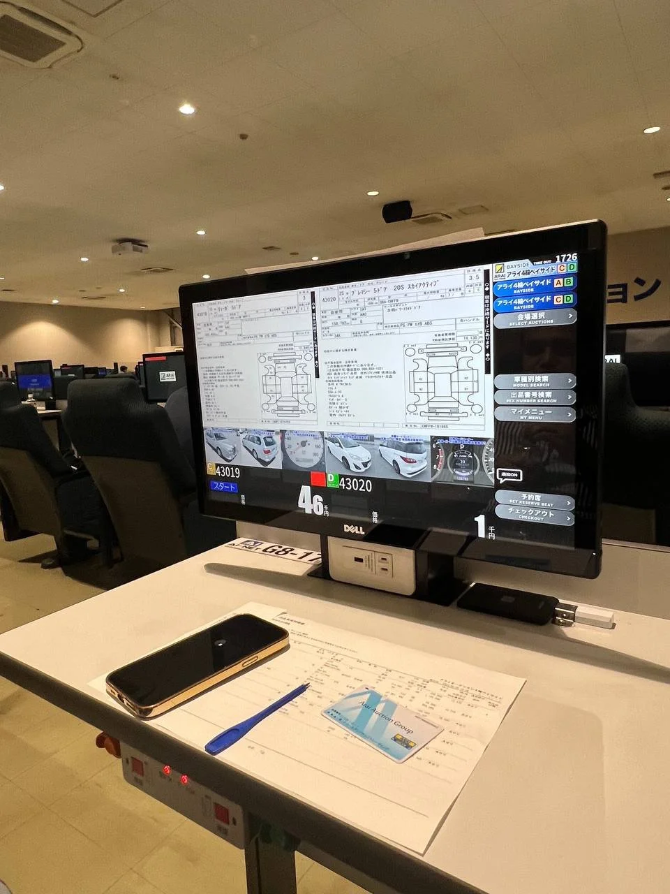 Airport check-in kiosk with flight and vehicle information, a smartphone, pen, and document on a desk, in a lounge area.