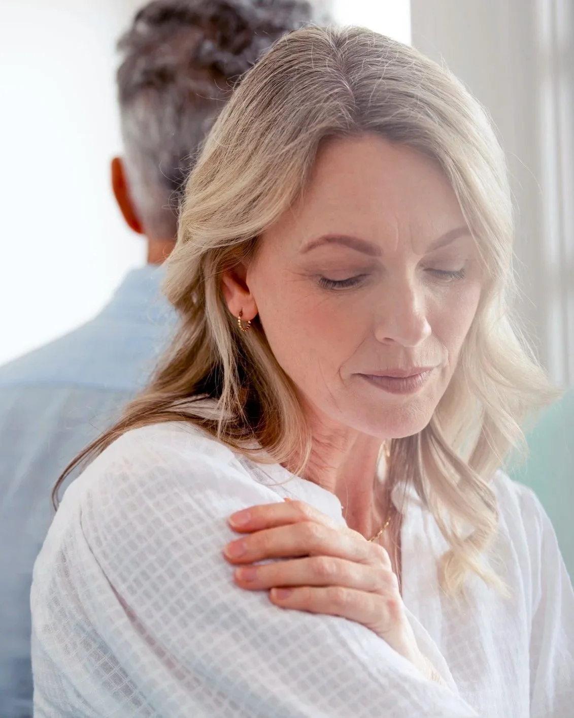 A woman with blonde hair, closed eyes, and a serious expression, standing with her arm crossed over her chest.