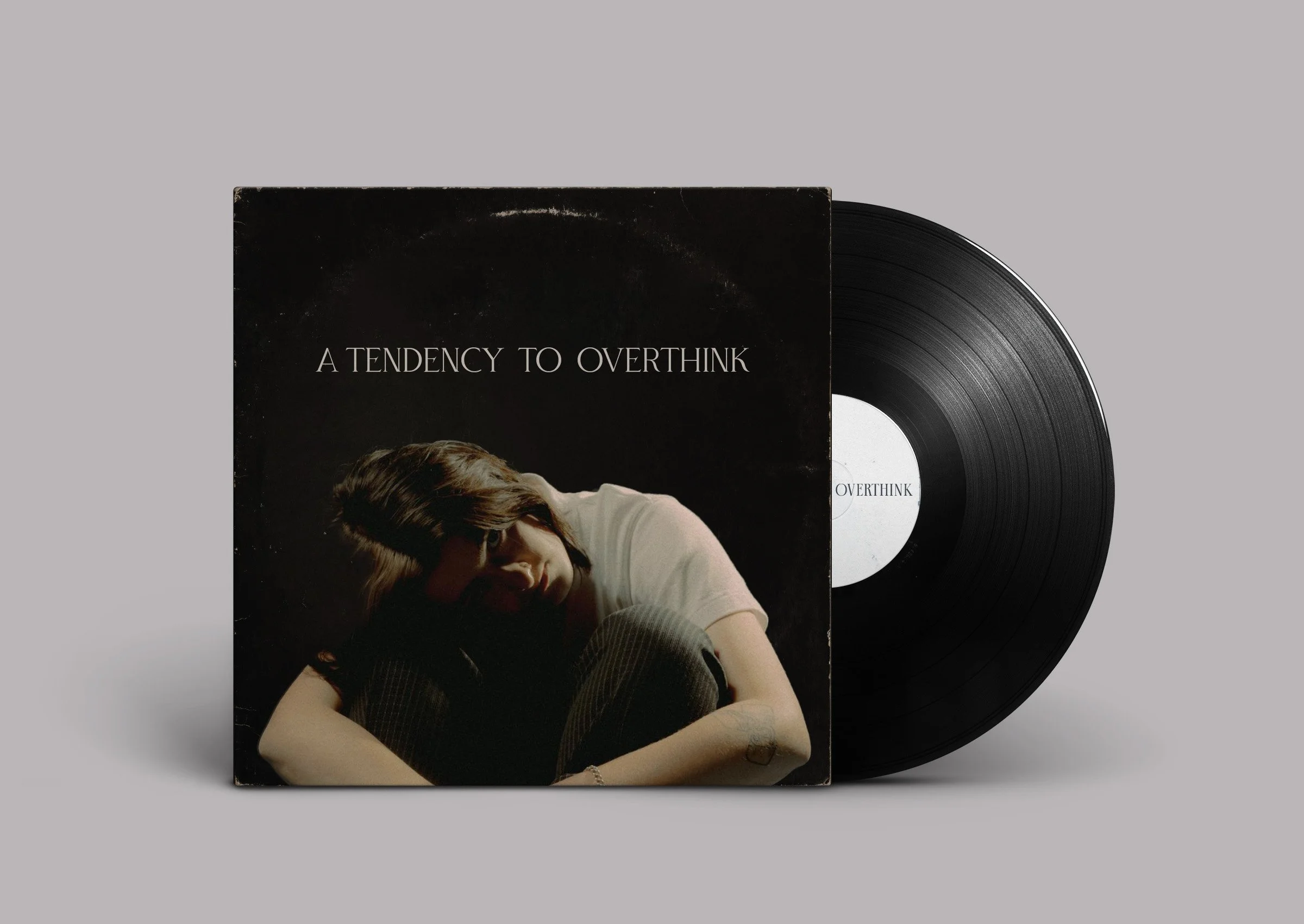 A vinyl record with a black cover featuring a woman with short hair sitting with her knees pulled to her chest, and the text 'A TENDENCY TO OVERTHINK' on the cover.