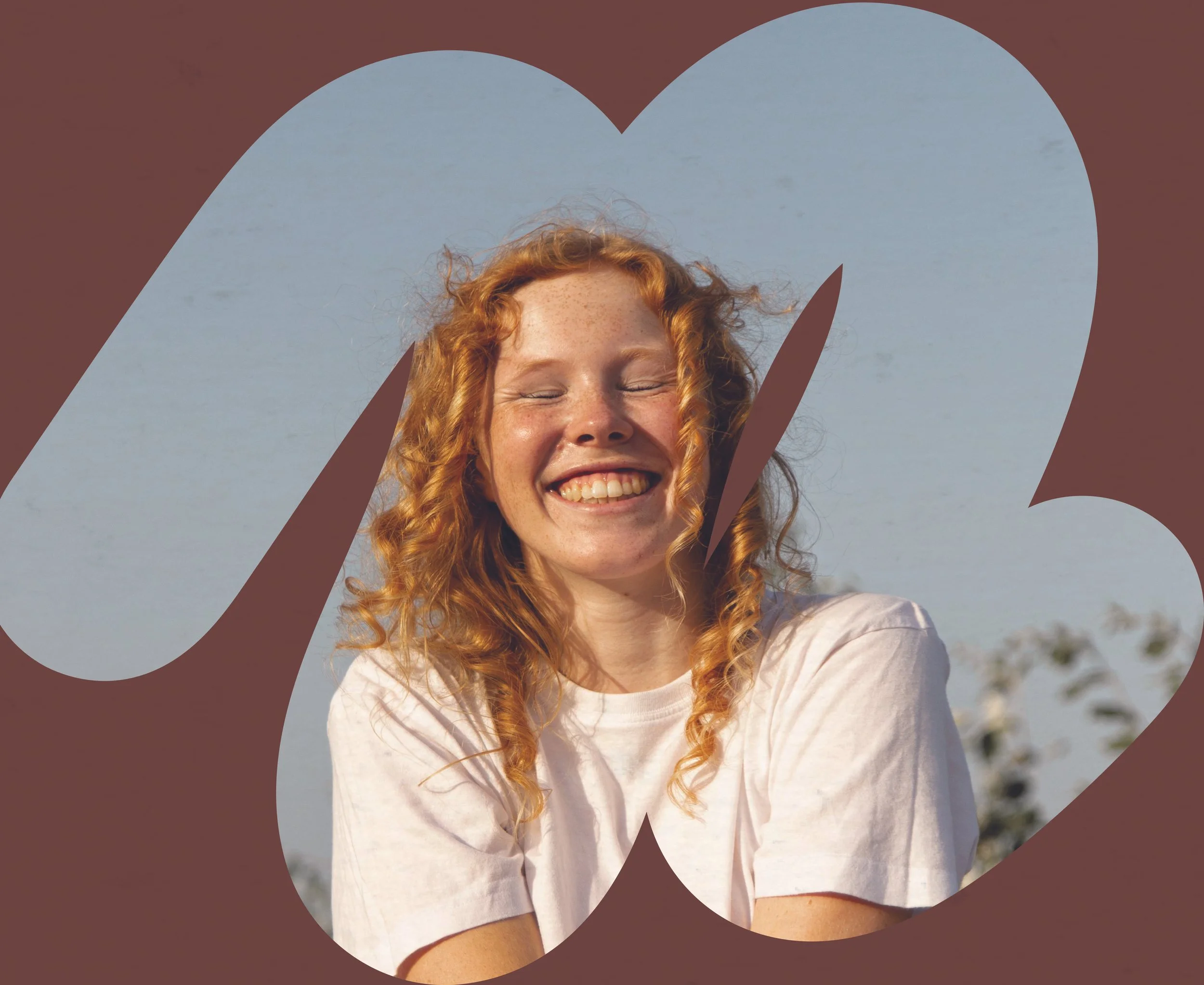 Smiling woman with curly red hair and light skin in a white shirt, outdoors against a cloudy sky.