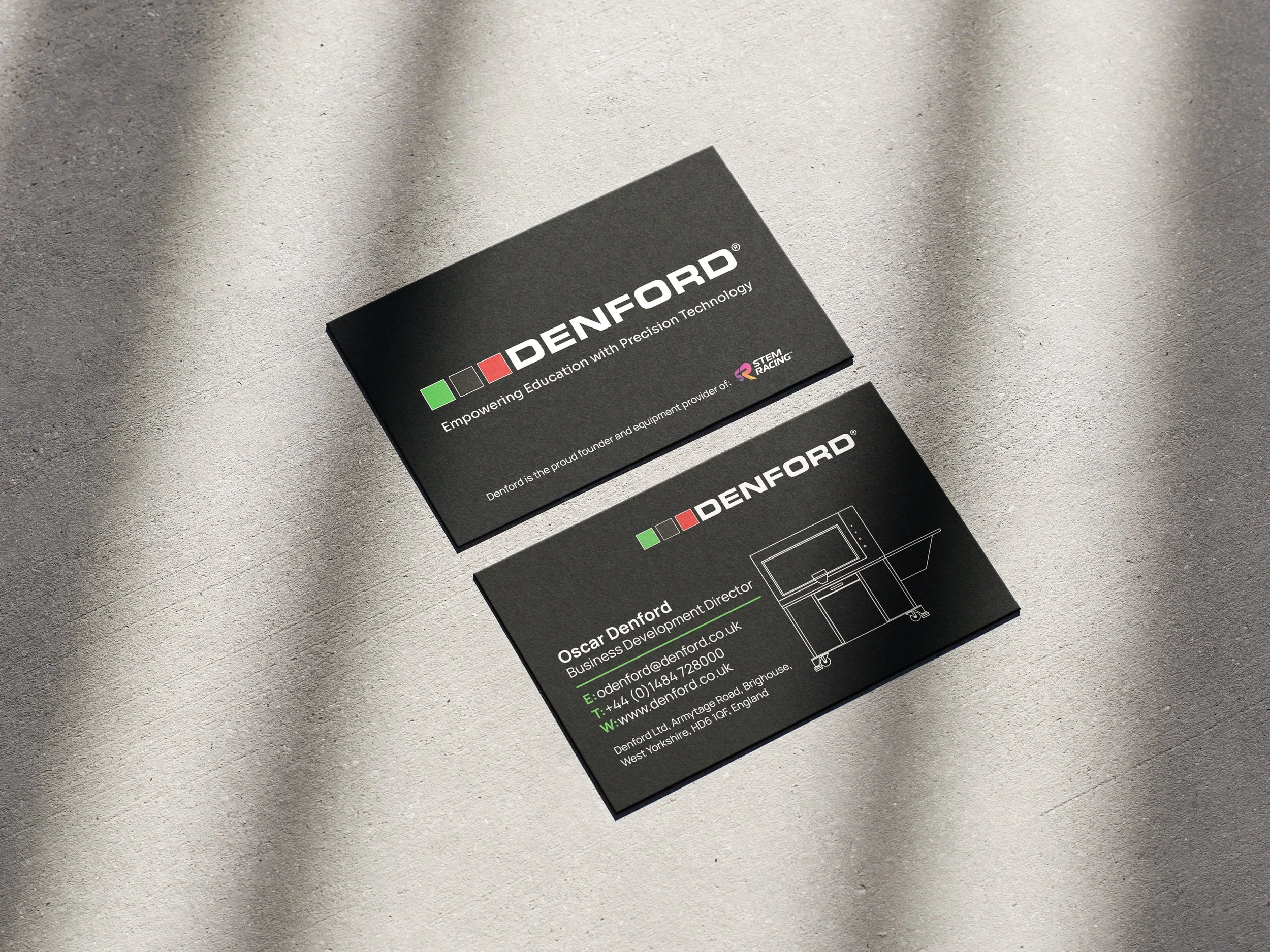 Two black business cards on a gray surface, with the Denford logo, contact information, and a technical drawing of a piece of equipment.