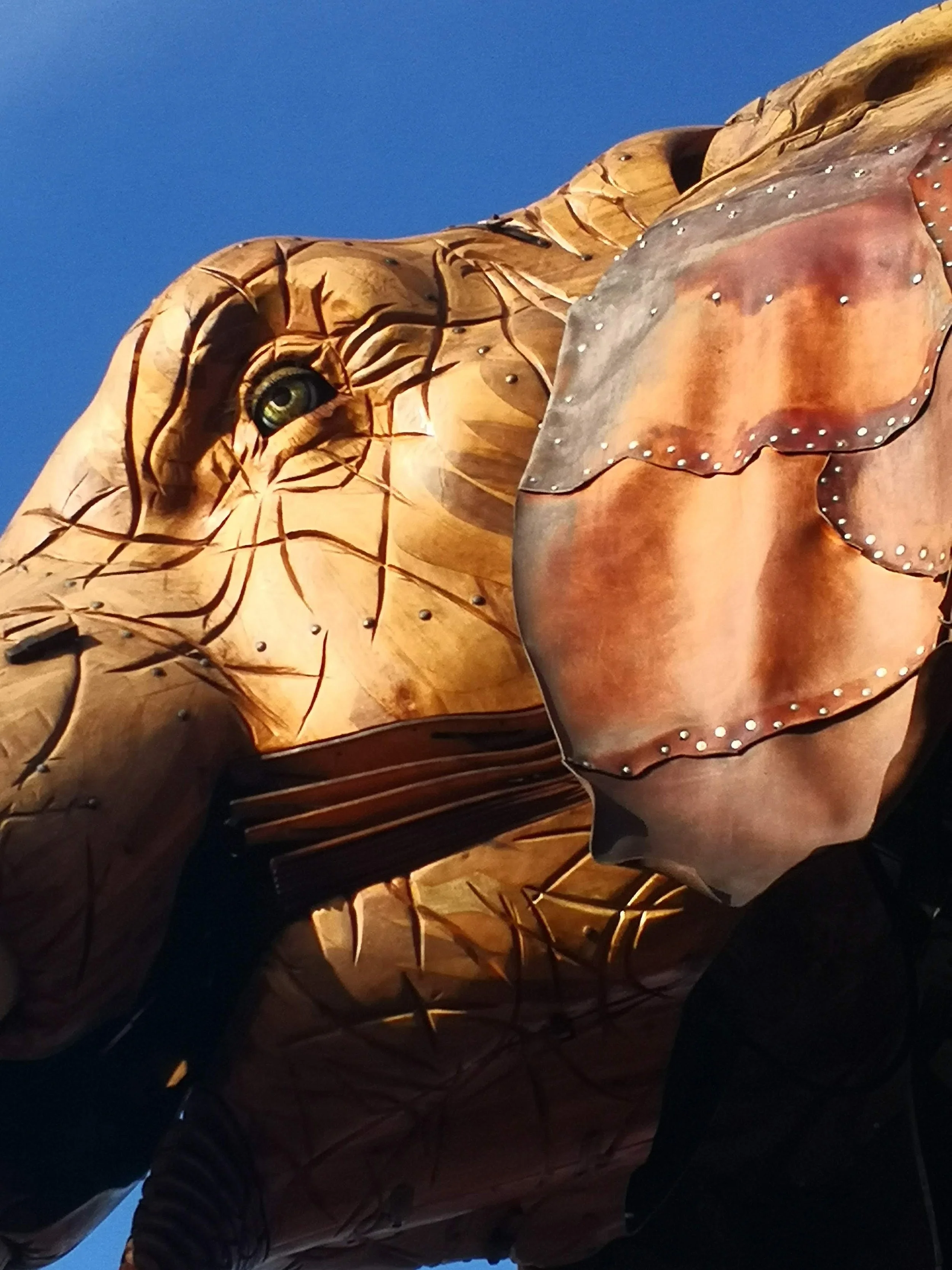 Grand cheval en wood art avec un masque en métal, sous un ciel bleu.