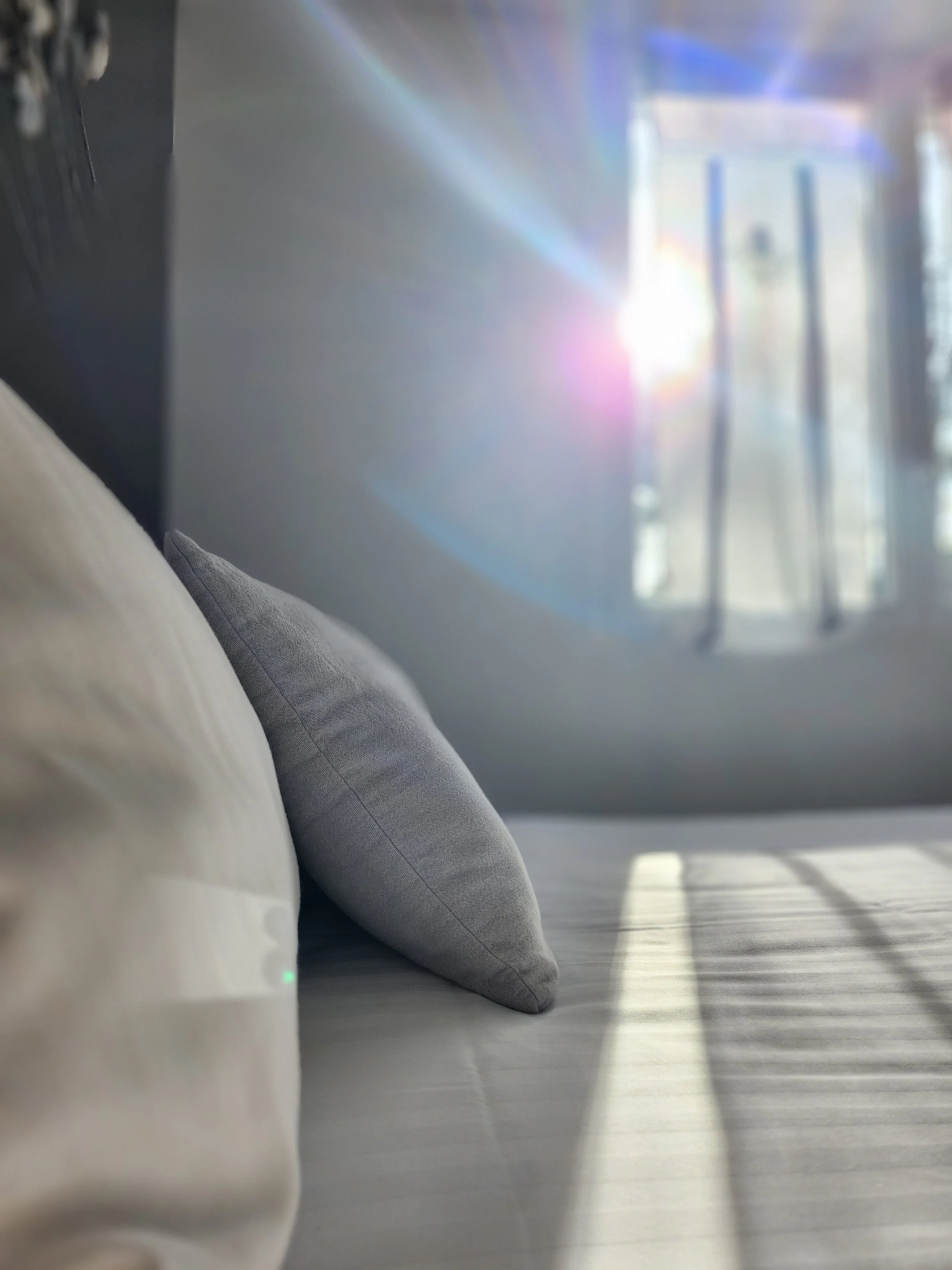 Coussin gris posé sur un lit ou un canapé avec la lumière du soleil qui entre à travers une fenêtre.