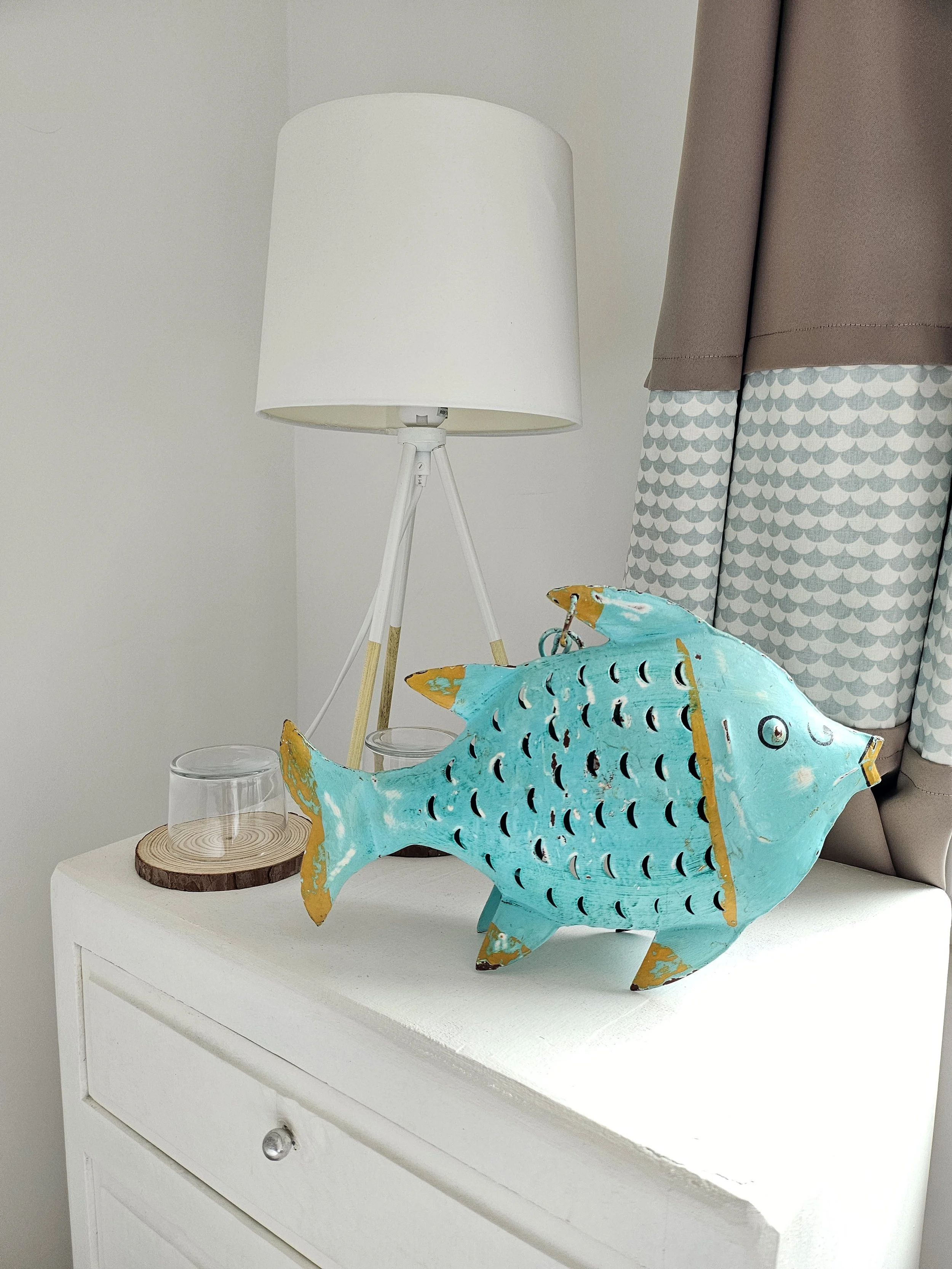 Elément décoration chambre enfant suite familiale Brevocean, poisson en métal peint en bleu avec des accents en or, avec une lampe blanche sur une petite table en arrière-plan.