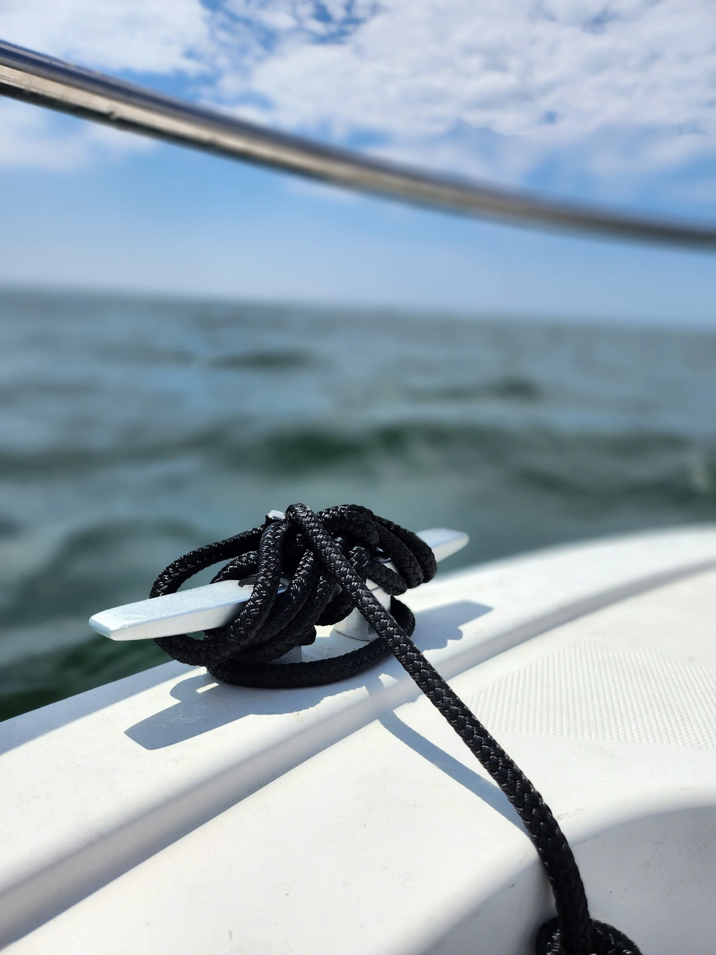 Corde noire attachée à une quille sur un bateau avec la mer et un ciel nuageux en arrière-plan, activité nautique en Loire-Atlantique. 