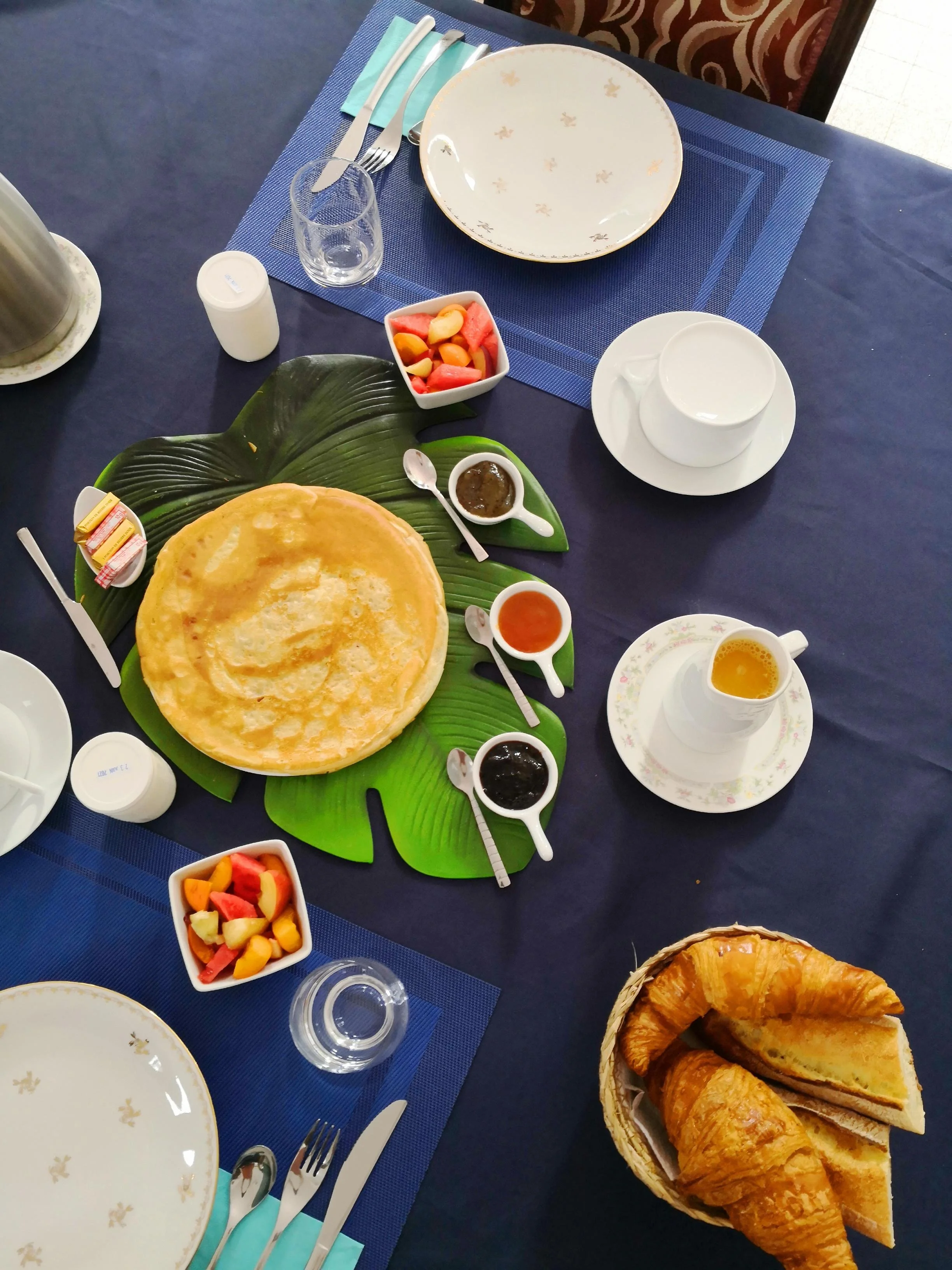 Petit-déjeuner d'hôtel soigneusement dressé avec des fruits coupés un croissant des crêpes des confitures maison jus d'orange frais pressé main yaourt maison et beure demi-sel