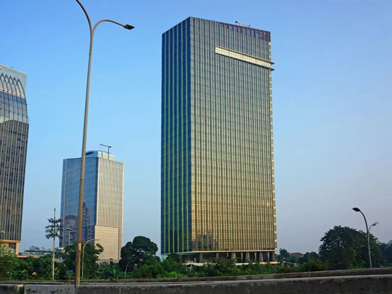 Cityscape with tall modern glass office buildings against a clear blue sky, with trees and streetlights in the foreground.