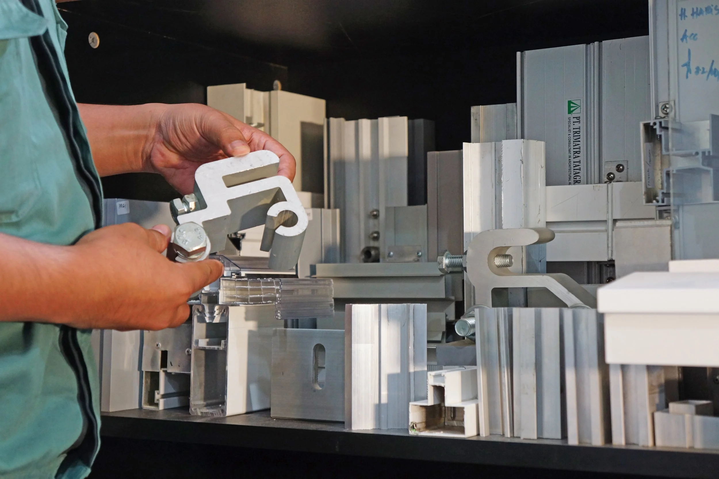 Person assembling aluminum mechanical parts on a metal surface with organized aluminum profiles in the background