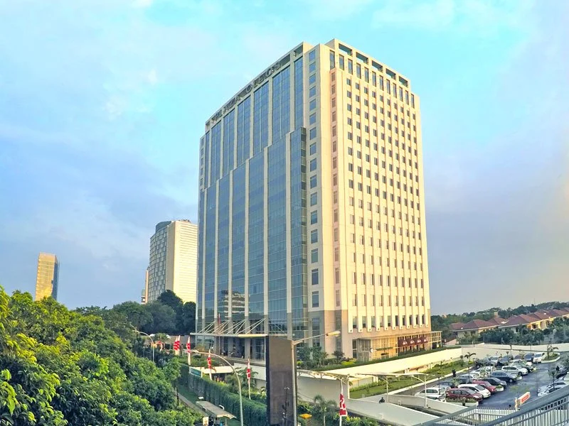 Tall modern office building with glass windows and a parking lot in the foreground.