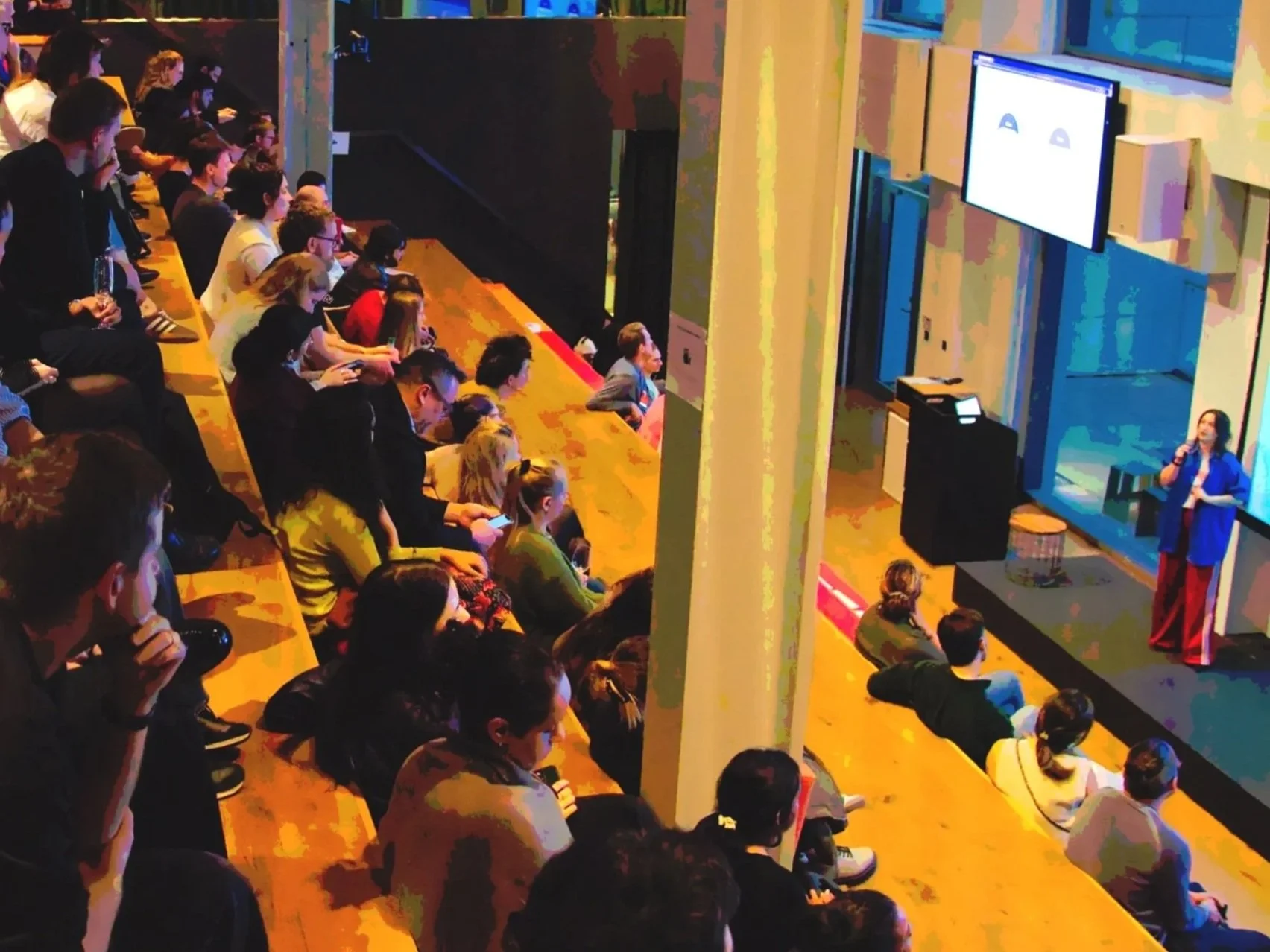 Alex speaking infront of a live audience that are raised on many levels giving a talk about AI in Be Kind Research.jpg