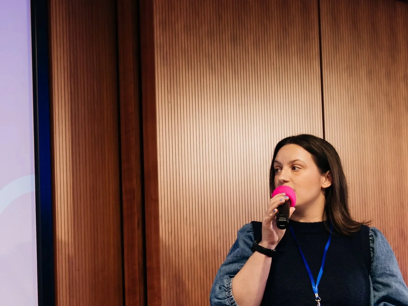 Alex standing next to a screen with a microphone in her hand and in front of an in-person audience giving a presentation