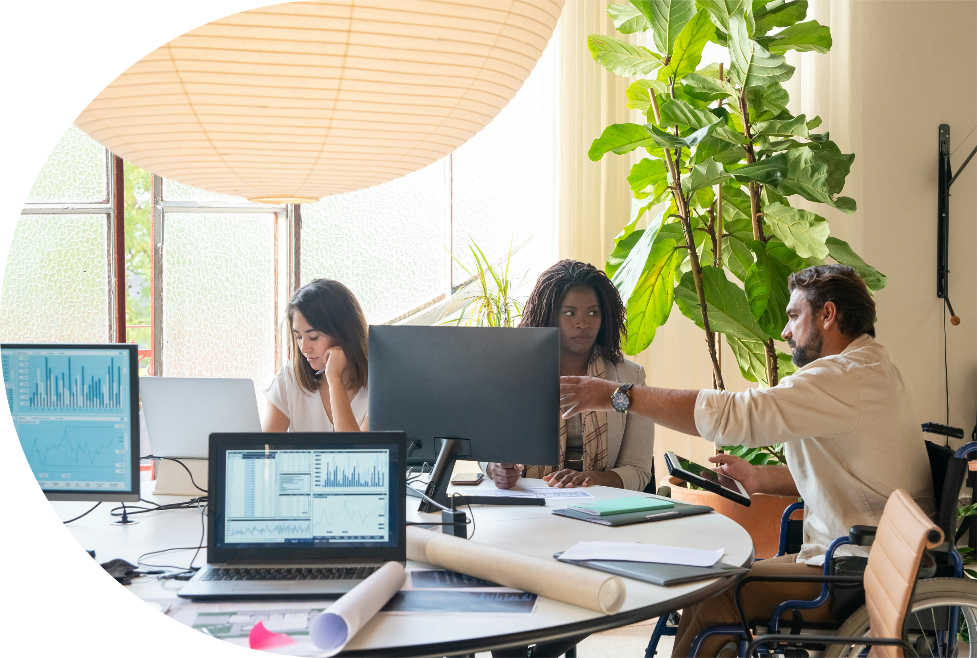 Une photo représentant un espace de travail. Des individus travaillent autour d'une table sur laquelle reposent des ordinateurs et des dossiers.