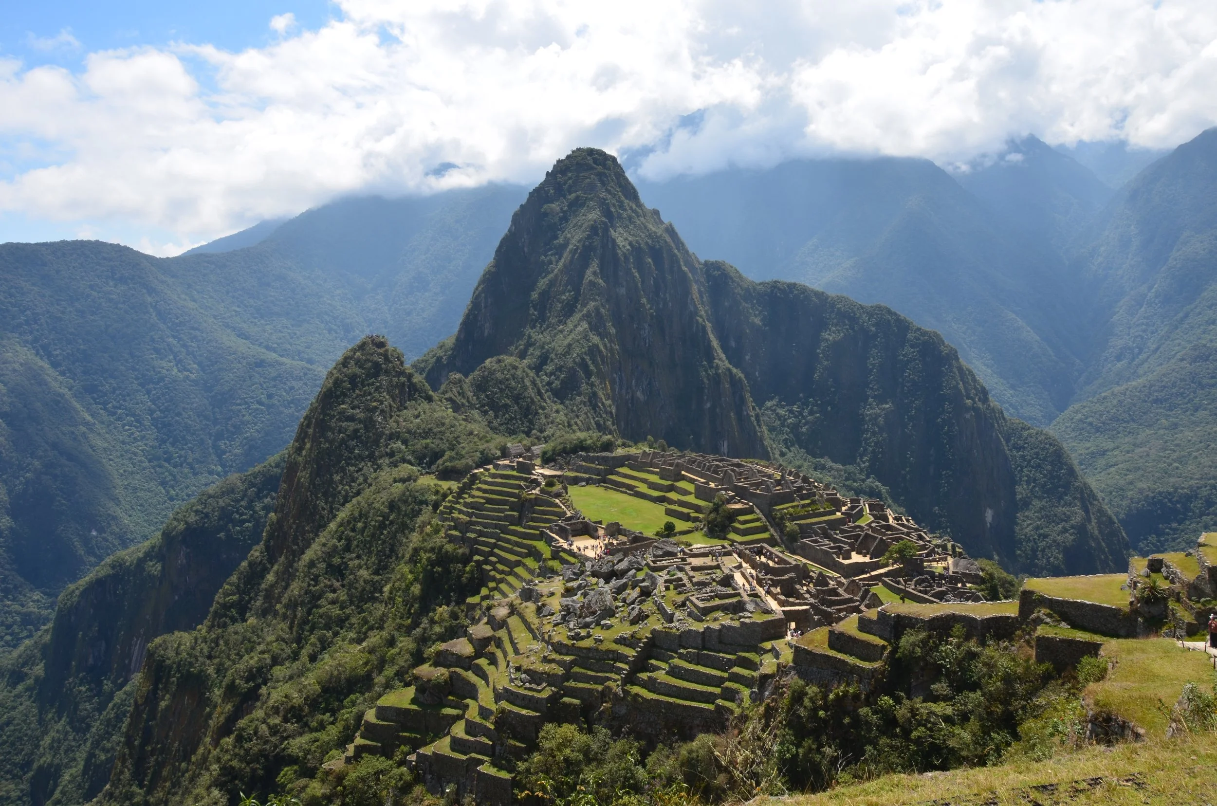 Ruines de Machu Picchu au sommet d'une montagne entourée de sommets verdoyants et de nuages dans un paysage andin.