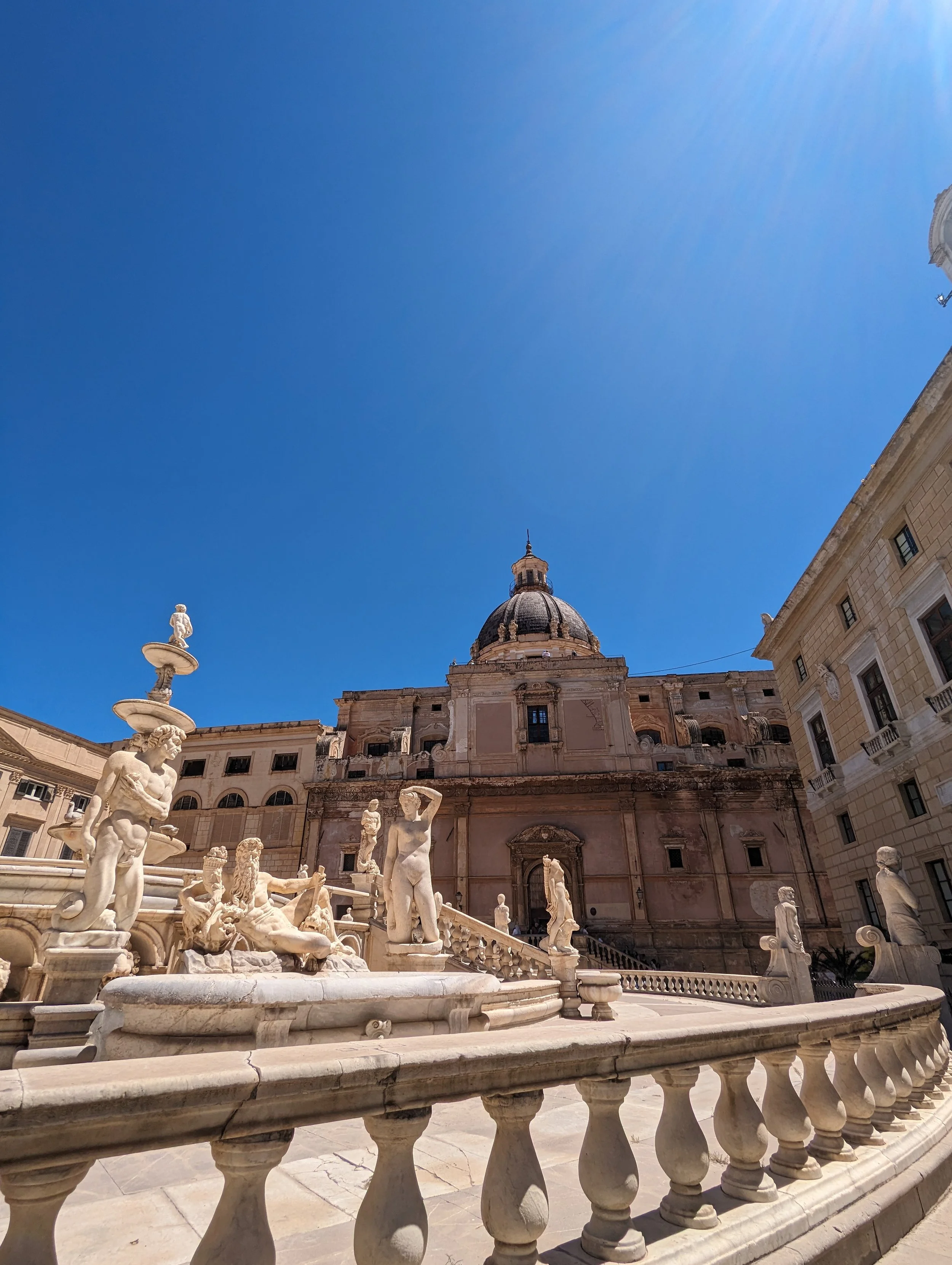 Fresque de statues en marbre devant un bâtiment ancien avec un dôme sous un ciel bleu.