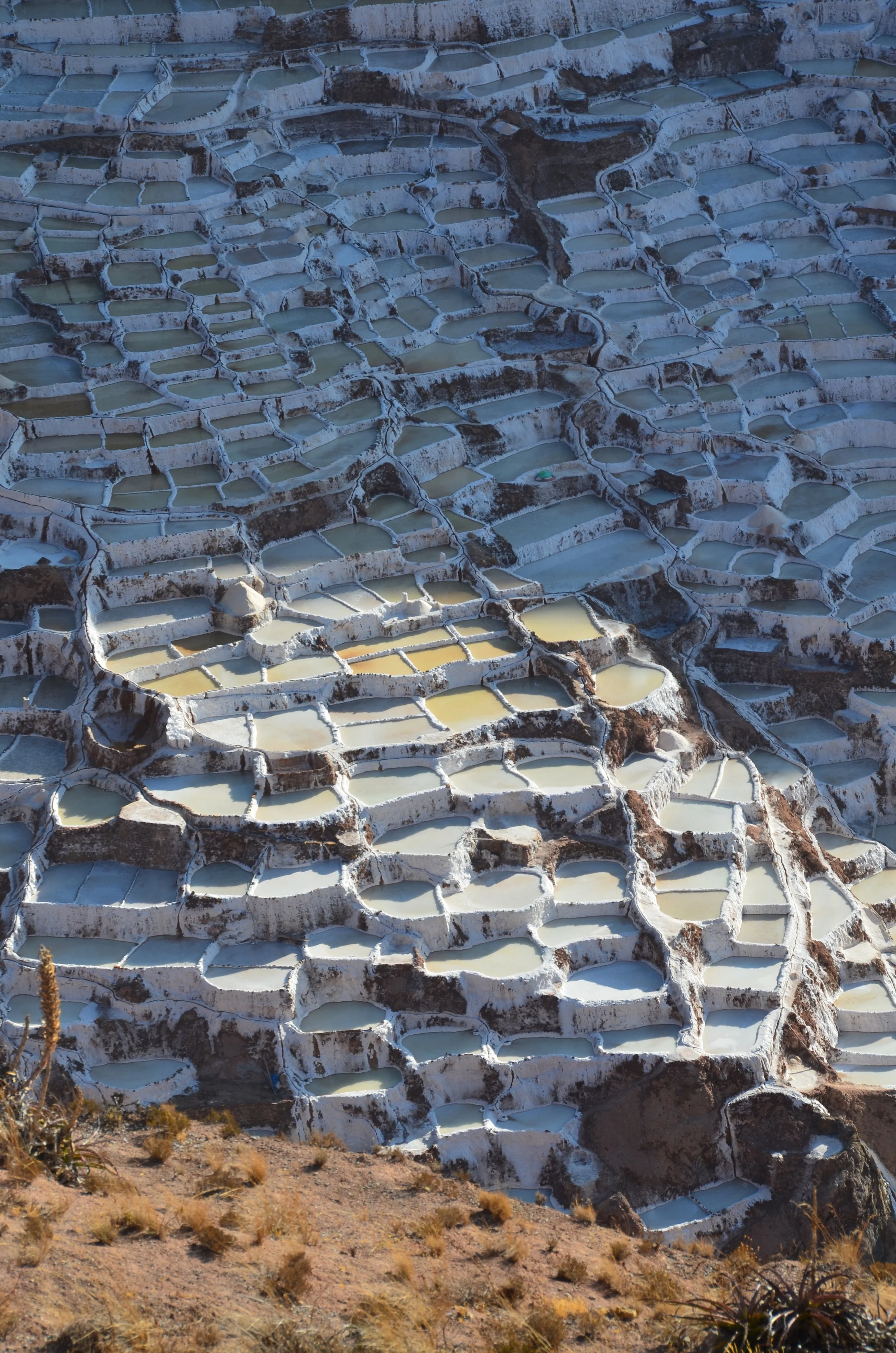 Terrasses de piscines naturelles de couleurs variées et formations rocheuses blanches dans un paysage montagneux aride.