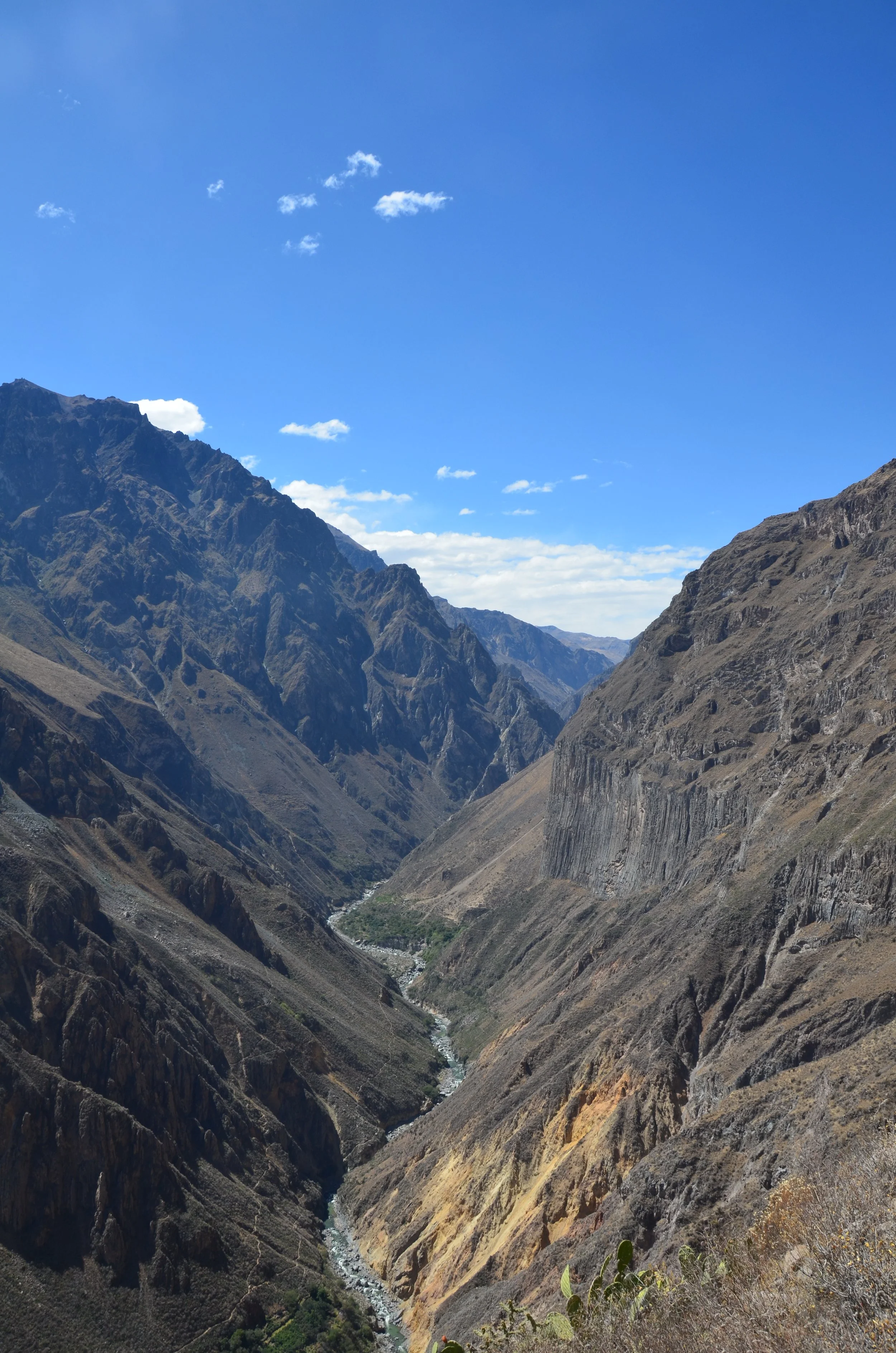 Vallée de montagnes escarpées sous un ciel bleu avec quelques nuages, rivière serpentant au fond.