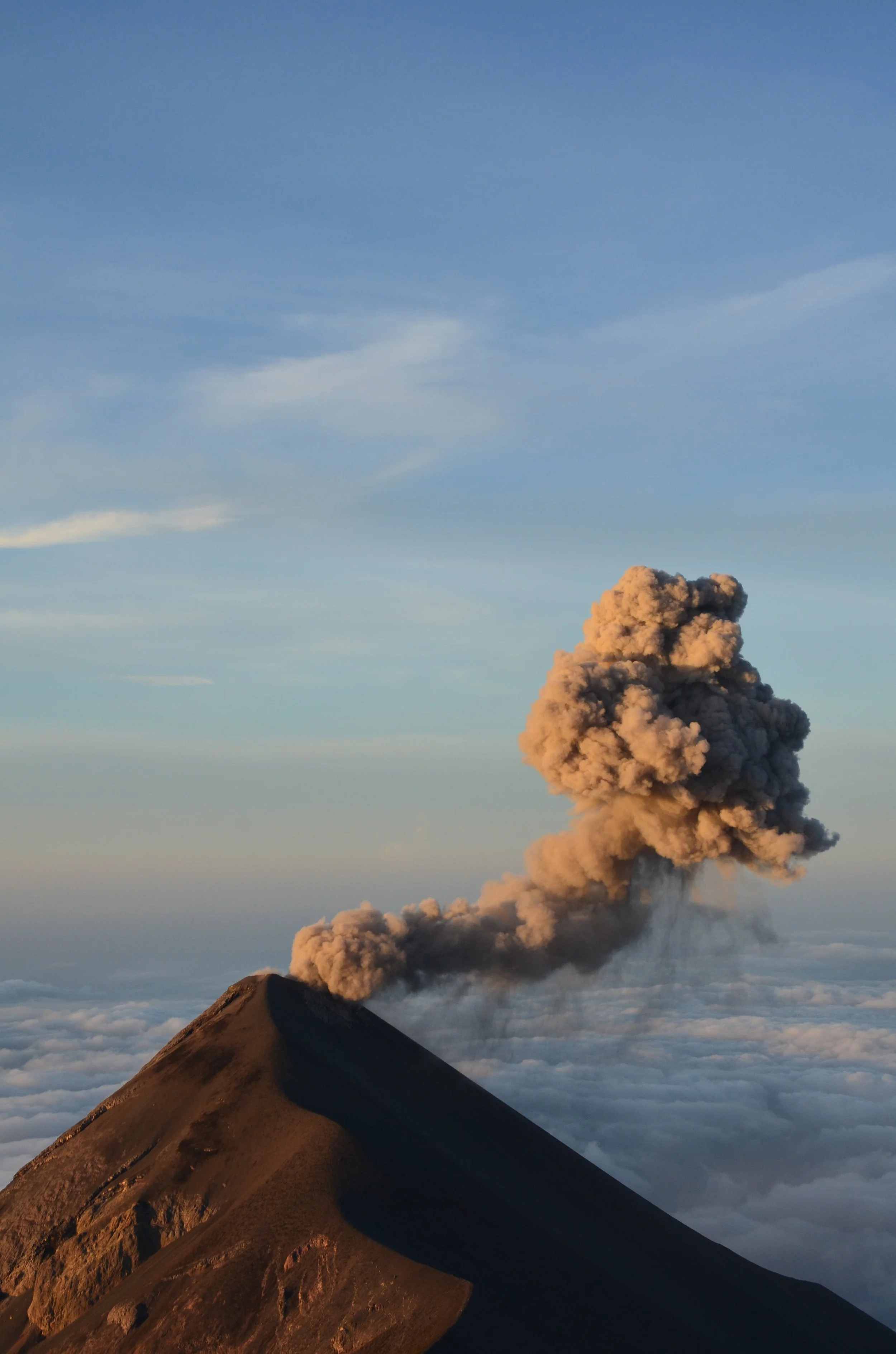Un volcan en éruption avec de la fumée sortant du sommet, au-dessus d'un ciel bleu et de nuages.