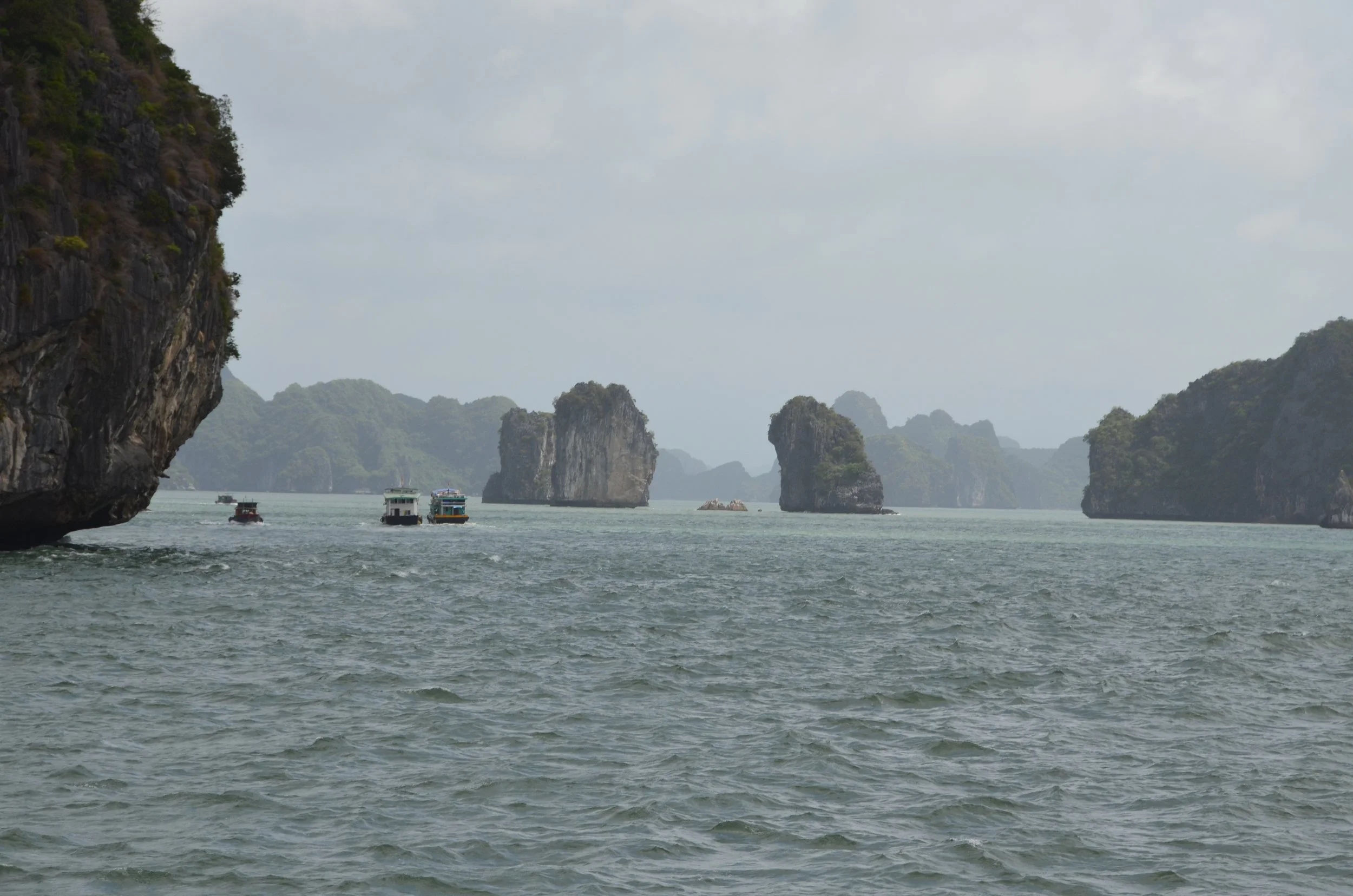 Vue d'une mer avec des falaises et des formations rocheuses et quelques bateaux naviguant.