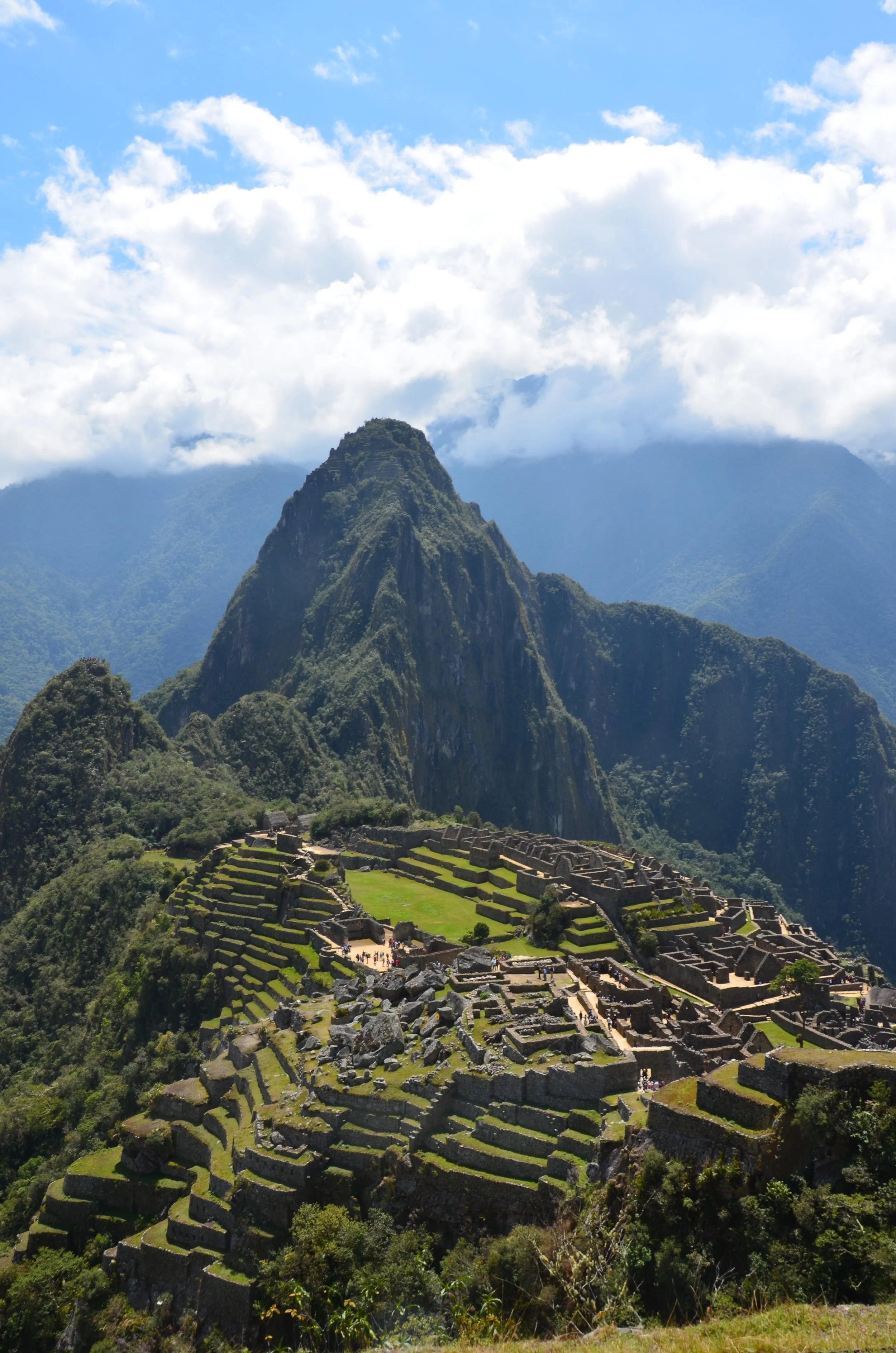 Ruines incas de Machu Picchu avec des terrasses vertes, montagne en arrière-plan, ciel bleu et nuages blancs