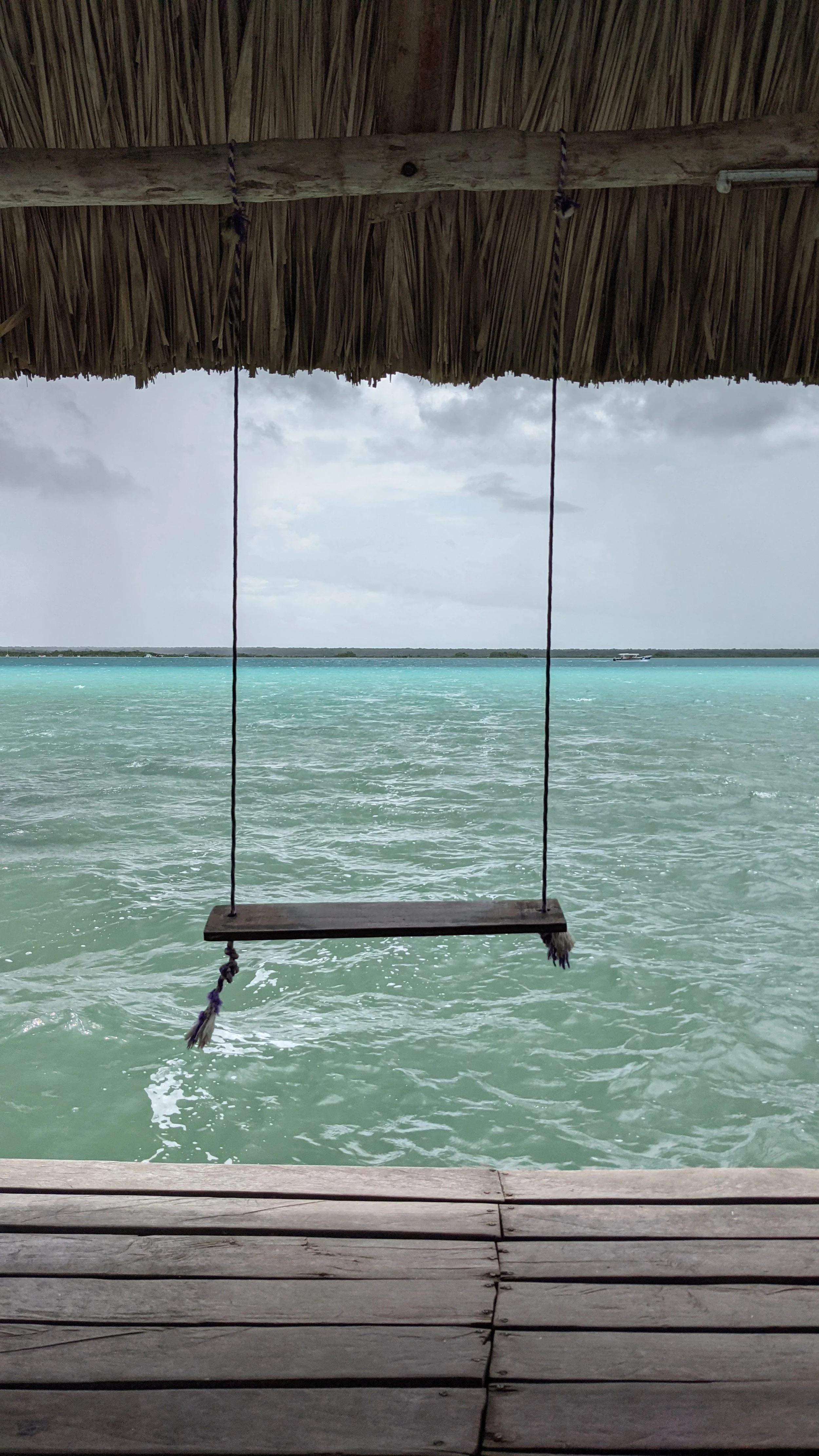 Balancier en bois suspendu devant une mer turquoise, sous un toit en chaume.