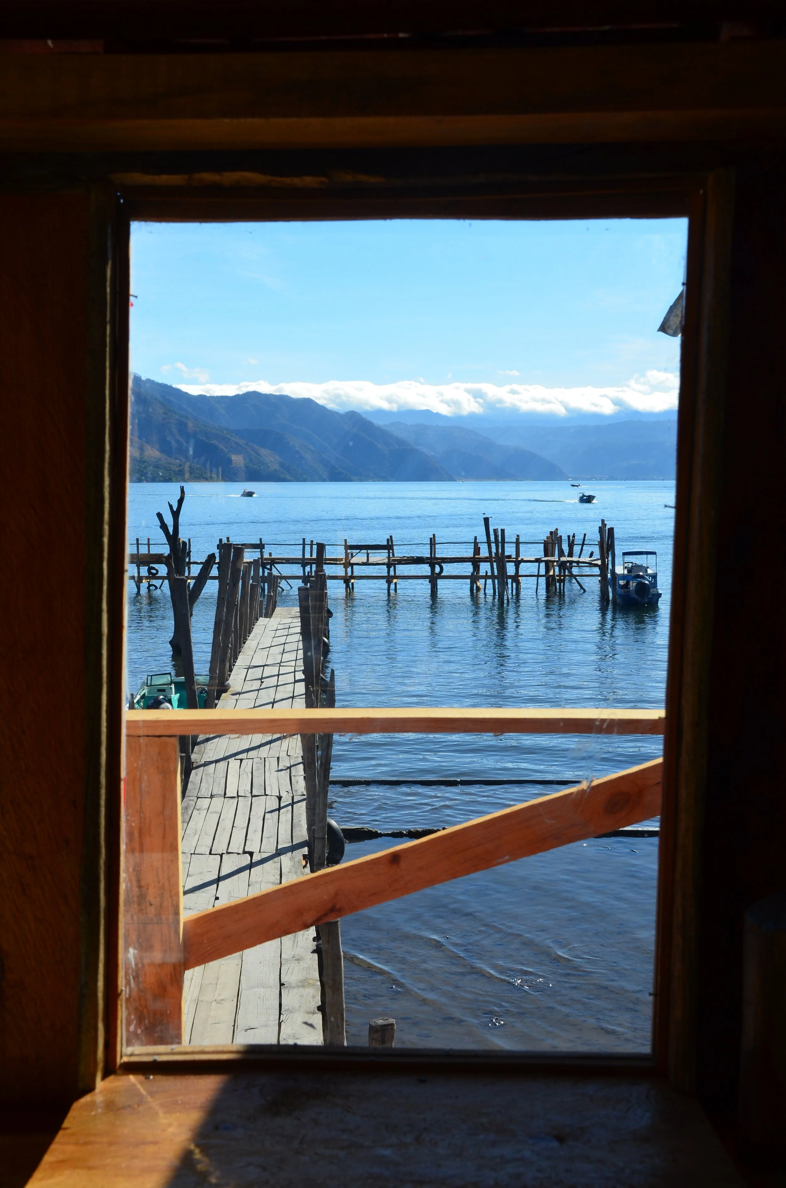 Vue d'un quai en bois menant à un lac avec des montagnes en arrière-plan, vue depuis une fenêtre