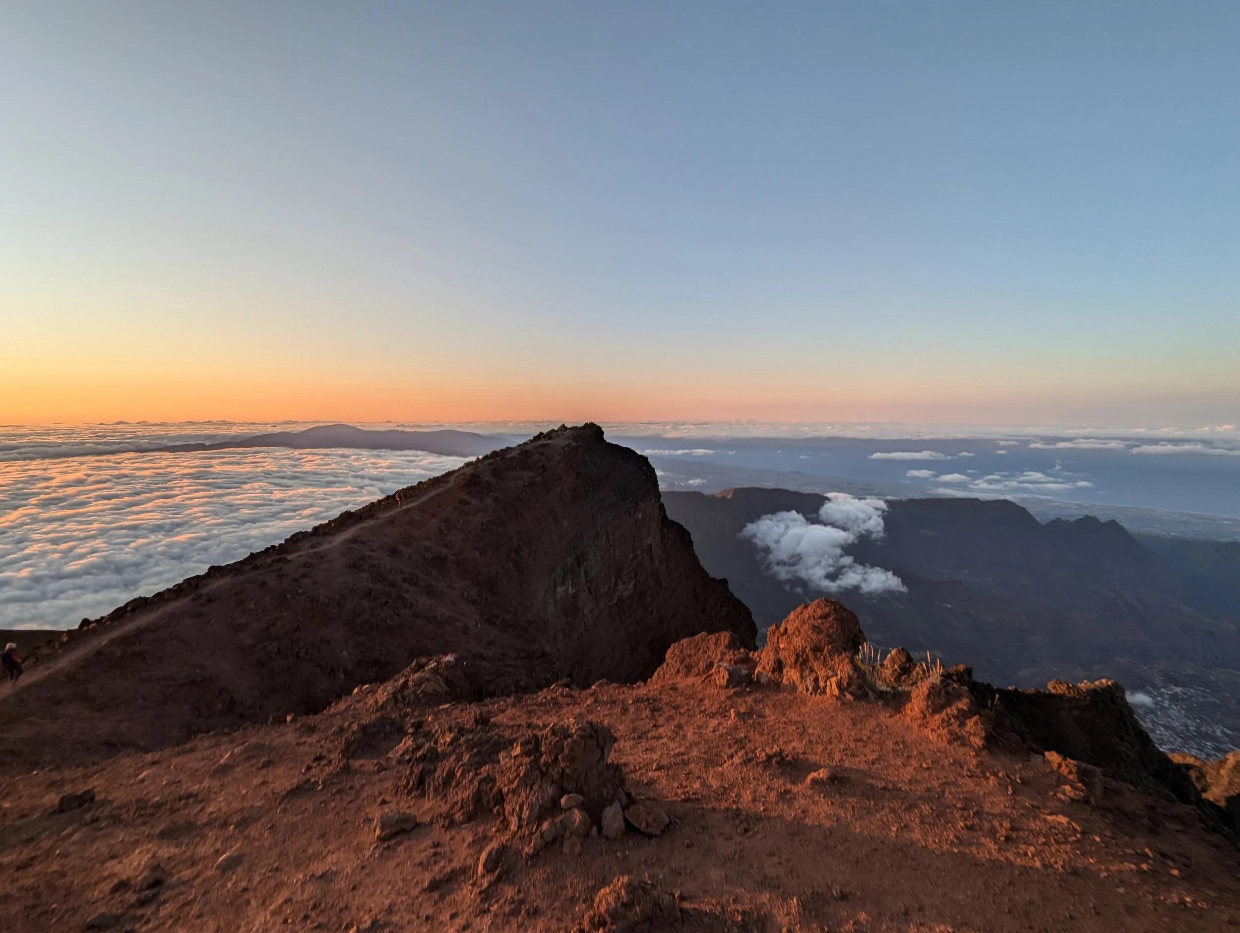 Vue d'une montagne au coucher du soleil avec des nuages en dessous et un ciel clair.