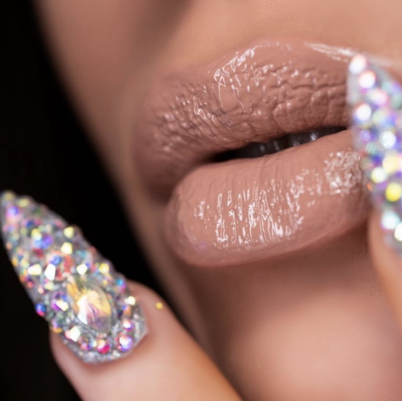 Close-up of glossy lips with crystal-embellished nail design