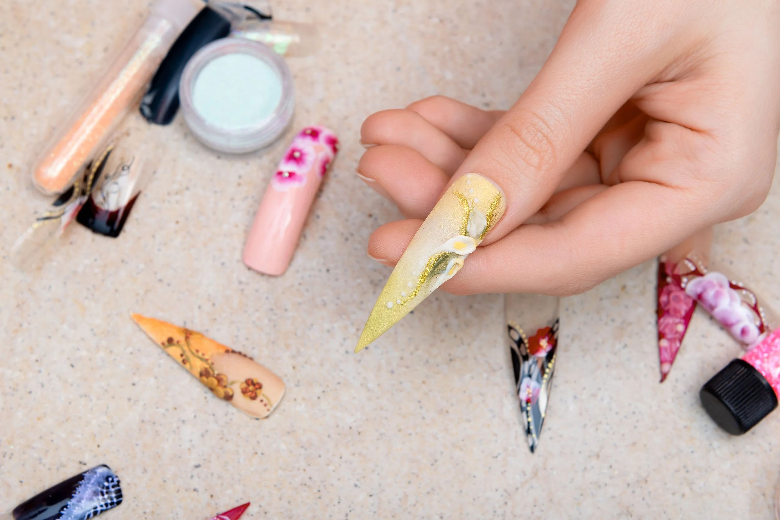 Hand holding a sculpted nail tip with detailed nail art design