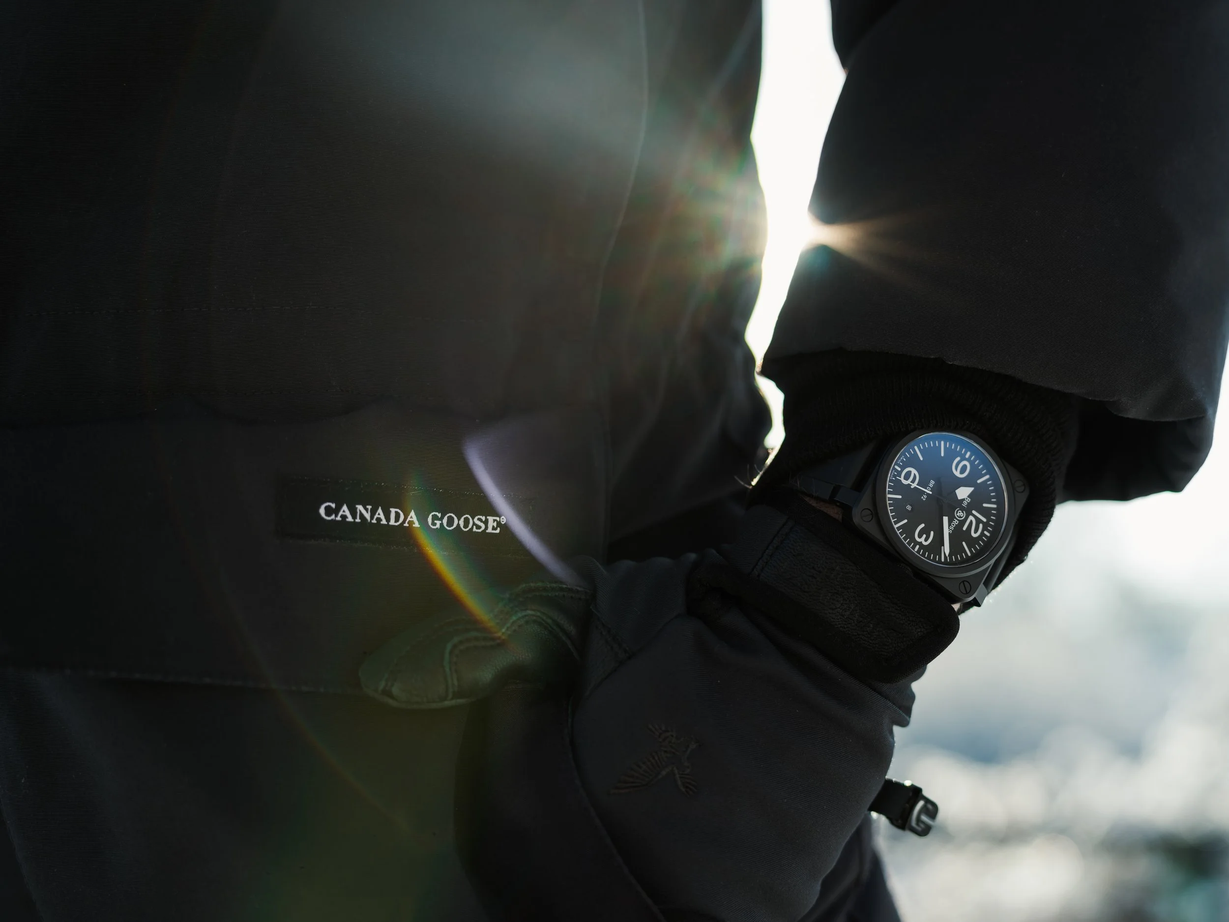 Close-up of a person's arm and wrist wearing a black Canada Goose jacket with a black Casio G-Shock watch, with sunlight in the background.