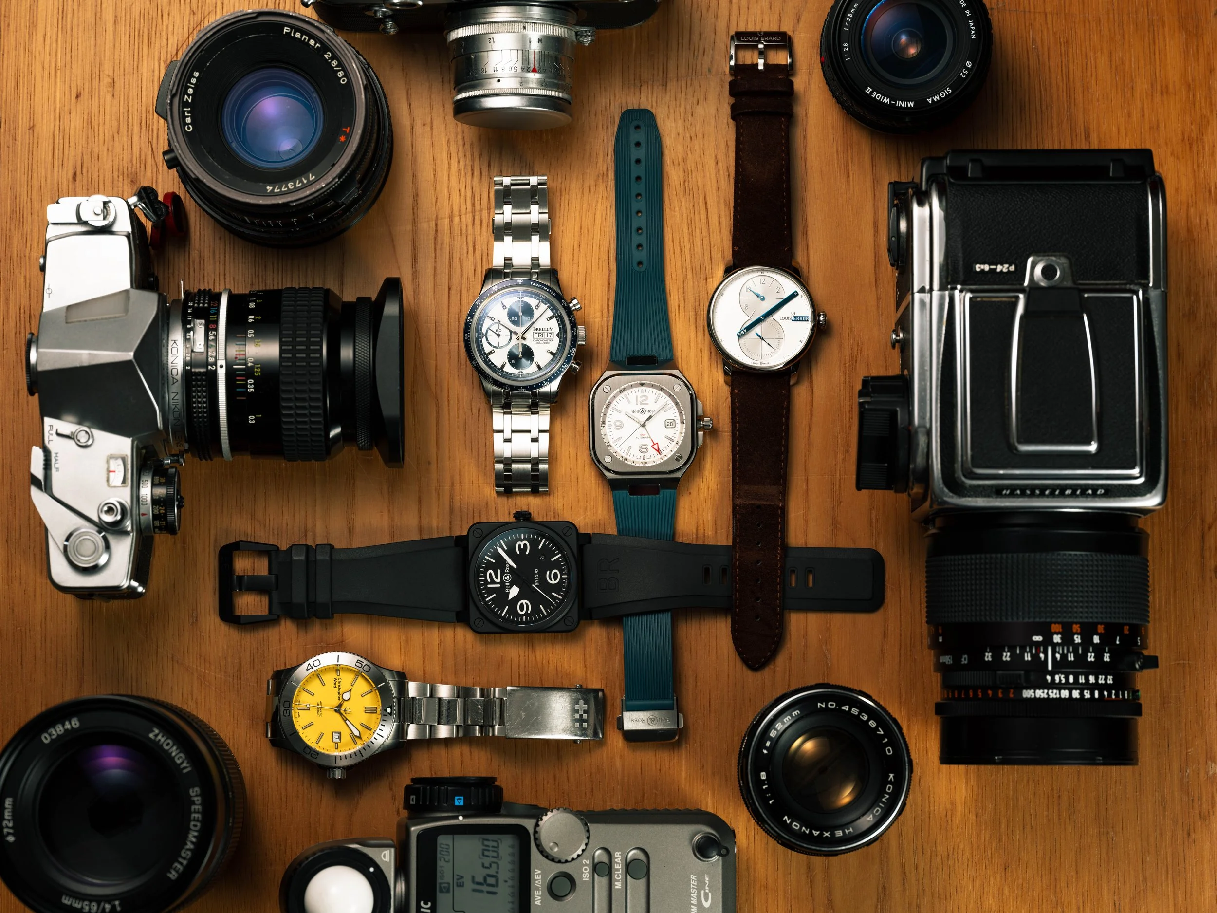 A collection of vintage cameras, lenses, and wristwatches arranged on a wooden surface.