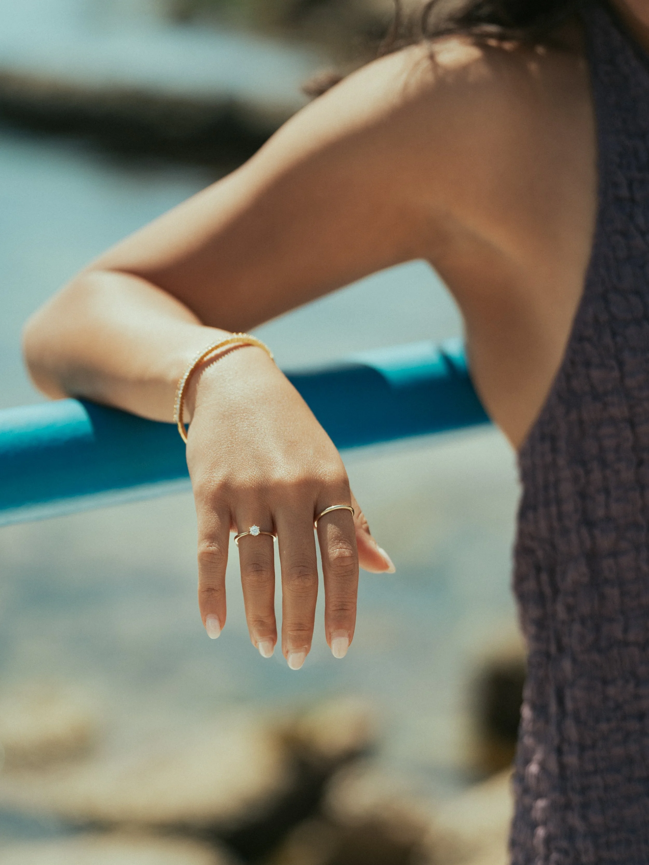 Close-up of a woman's hand with jewelry, resting on a blue railing at the beach.