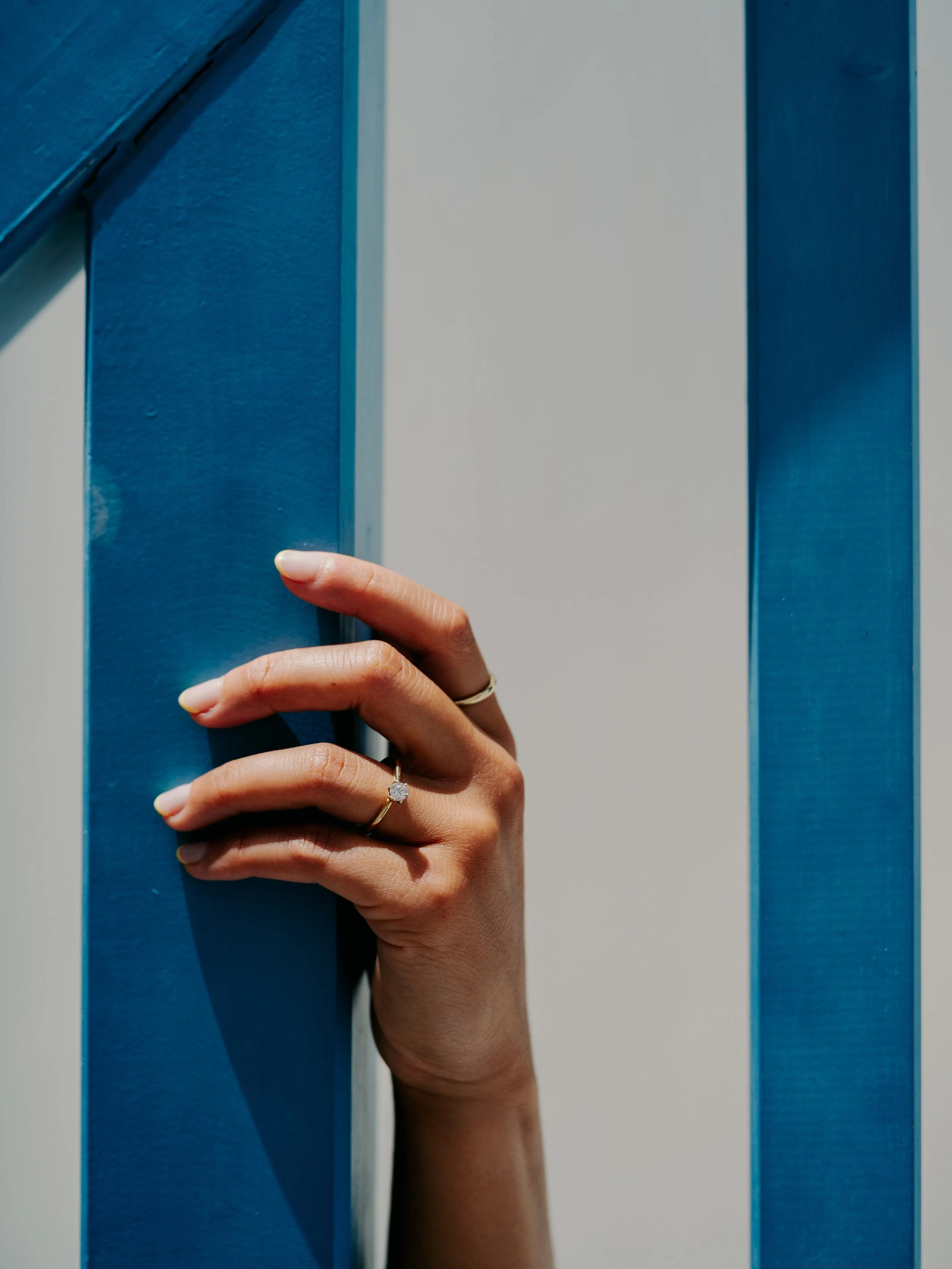 Close-up of a woman's hand with rings, touching a blue wall with vertical slats.